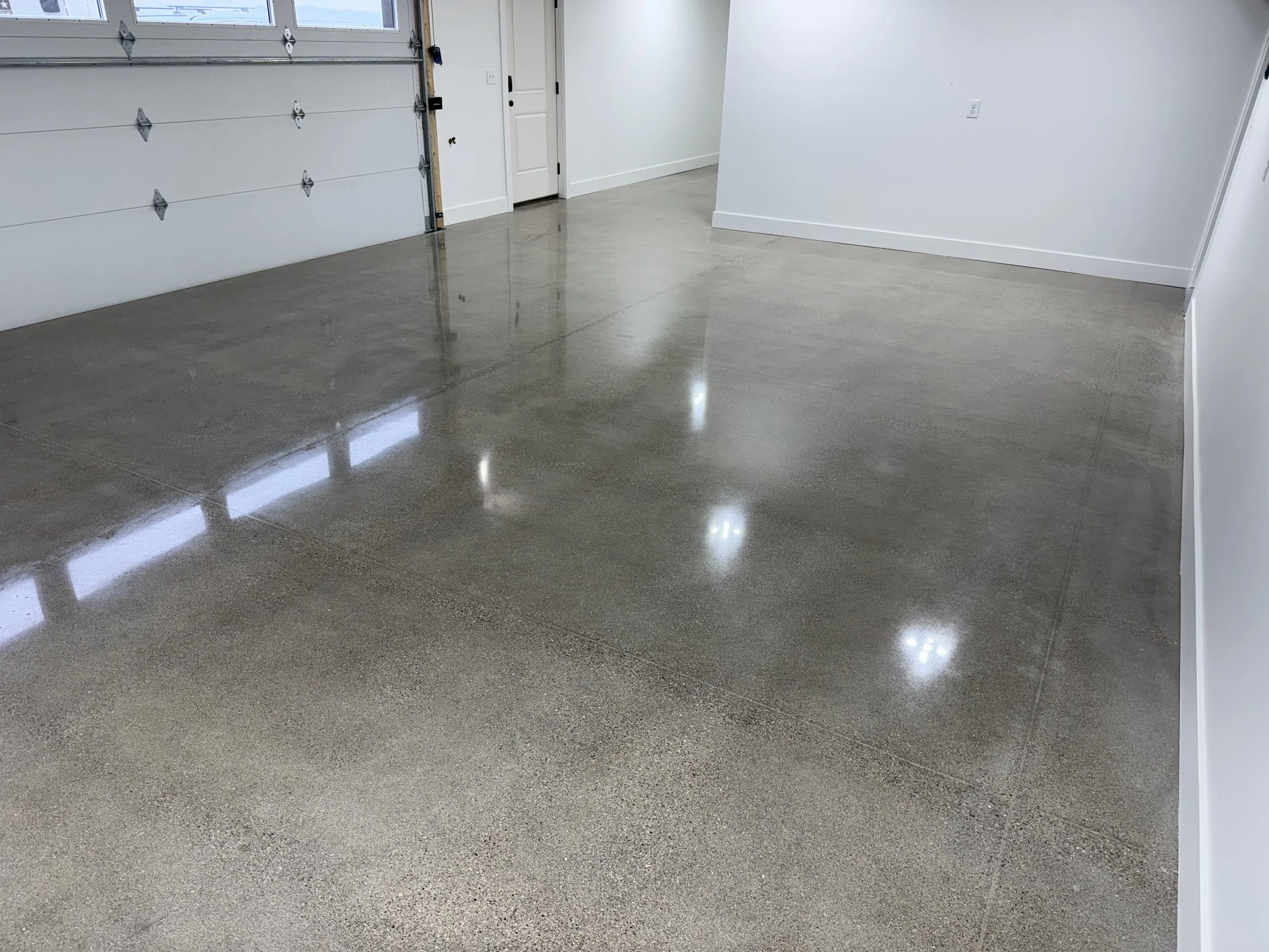 Empty garage with polished concrete floor, white walls, and a white garage door.