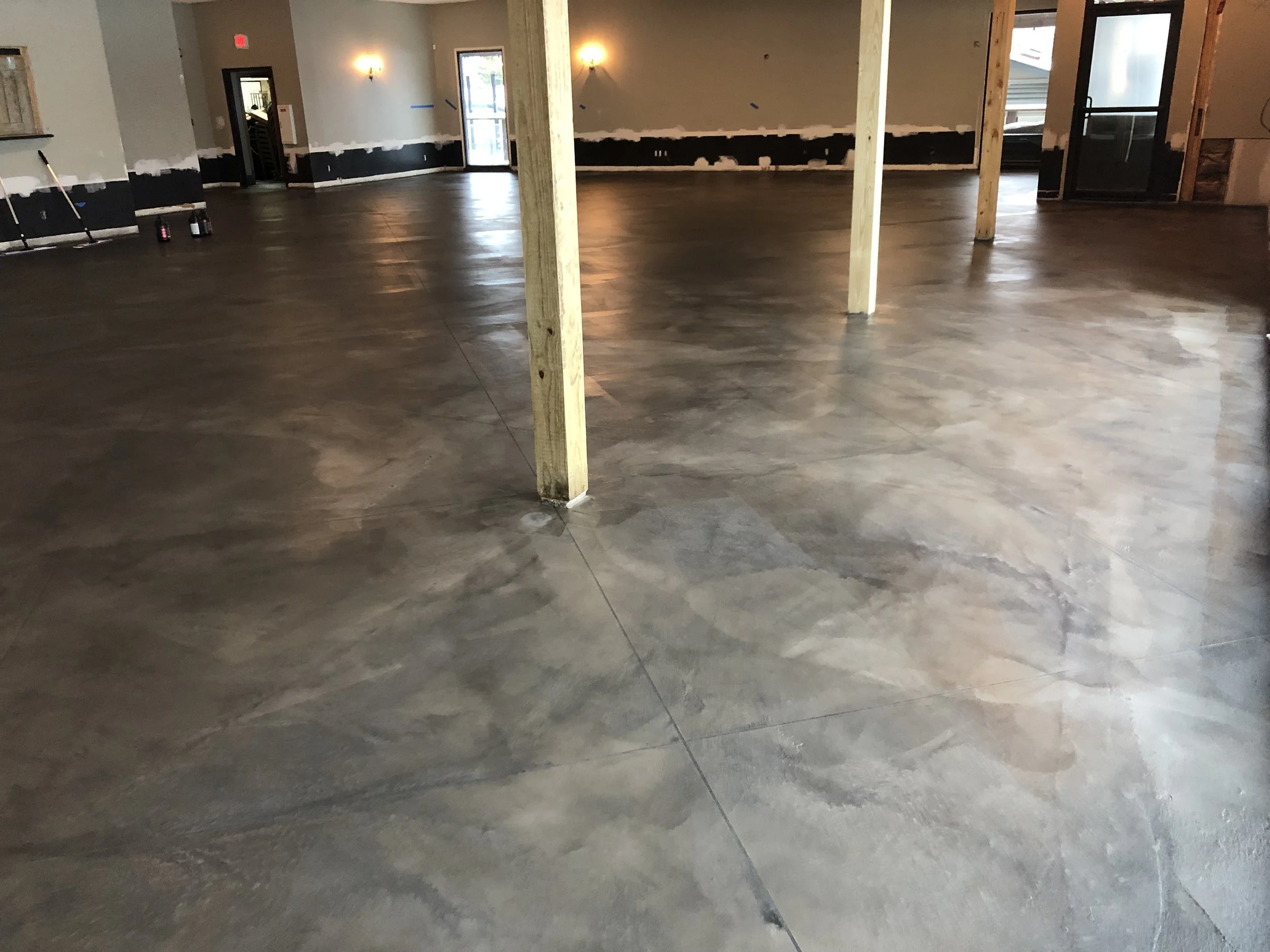Interior of a building under renovation with polished concrete floors, exposed wooden support beams, and unfinished walls with black trim along the bottom.
