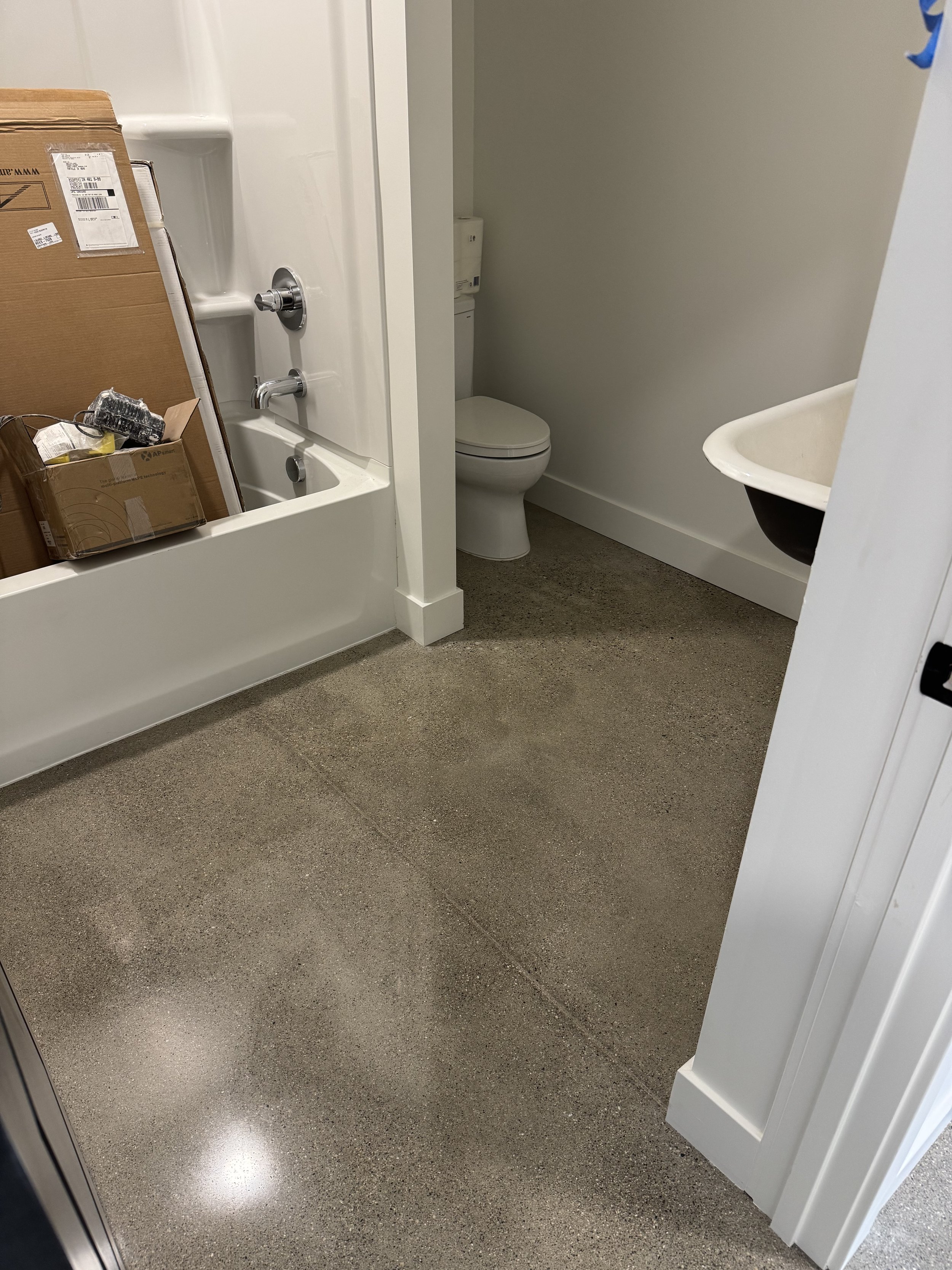 Bathroom with a toilet, a small sink, and a shower area with cardboard boxes inside.