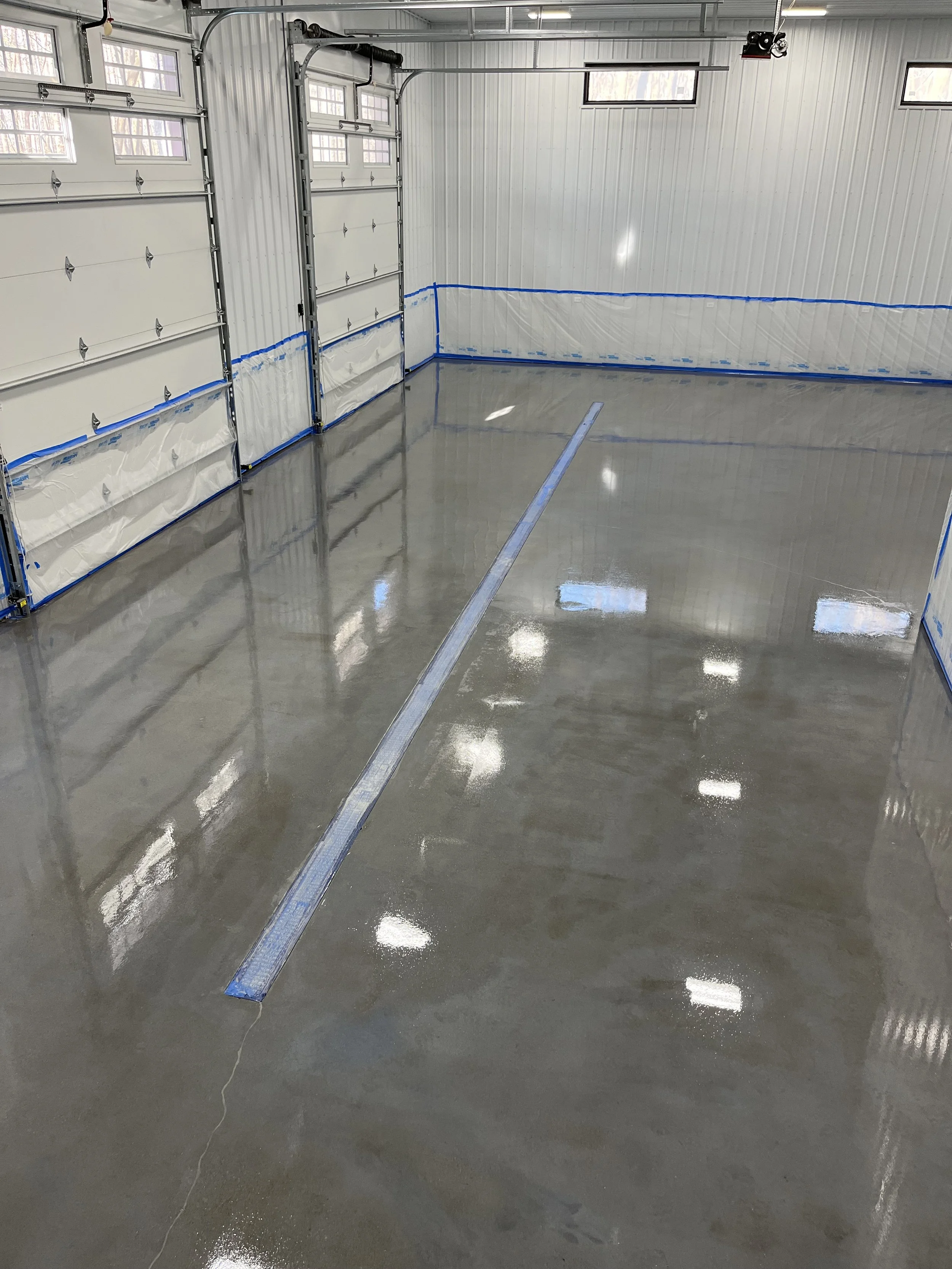 Clean, freshly poured concrete floor inside a spacious garage with metal walls and high windows, featuring a drain in the center.