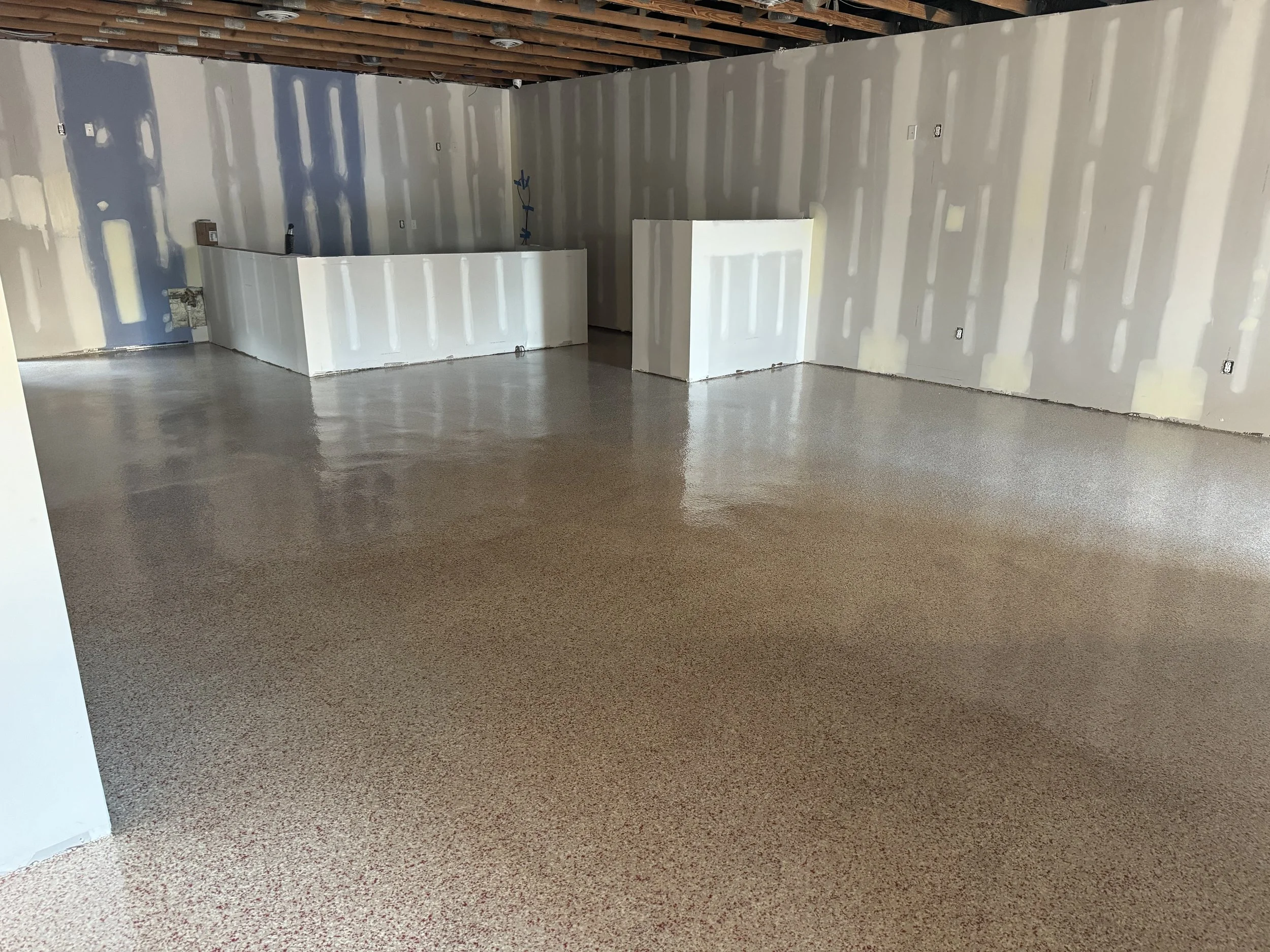 Empty room under construction with drywalled walls, exposed ceiling beams, and a polished epoxy floor.