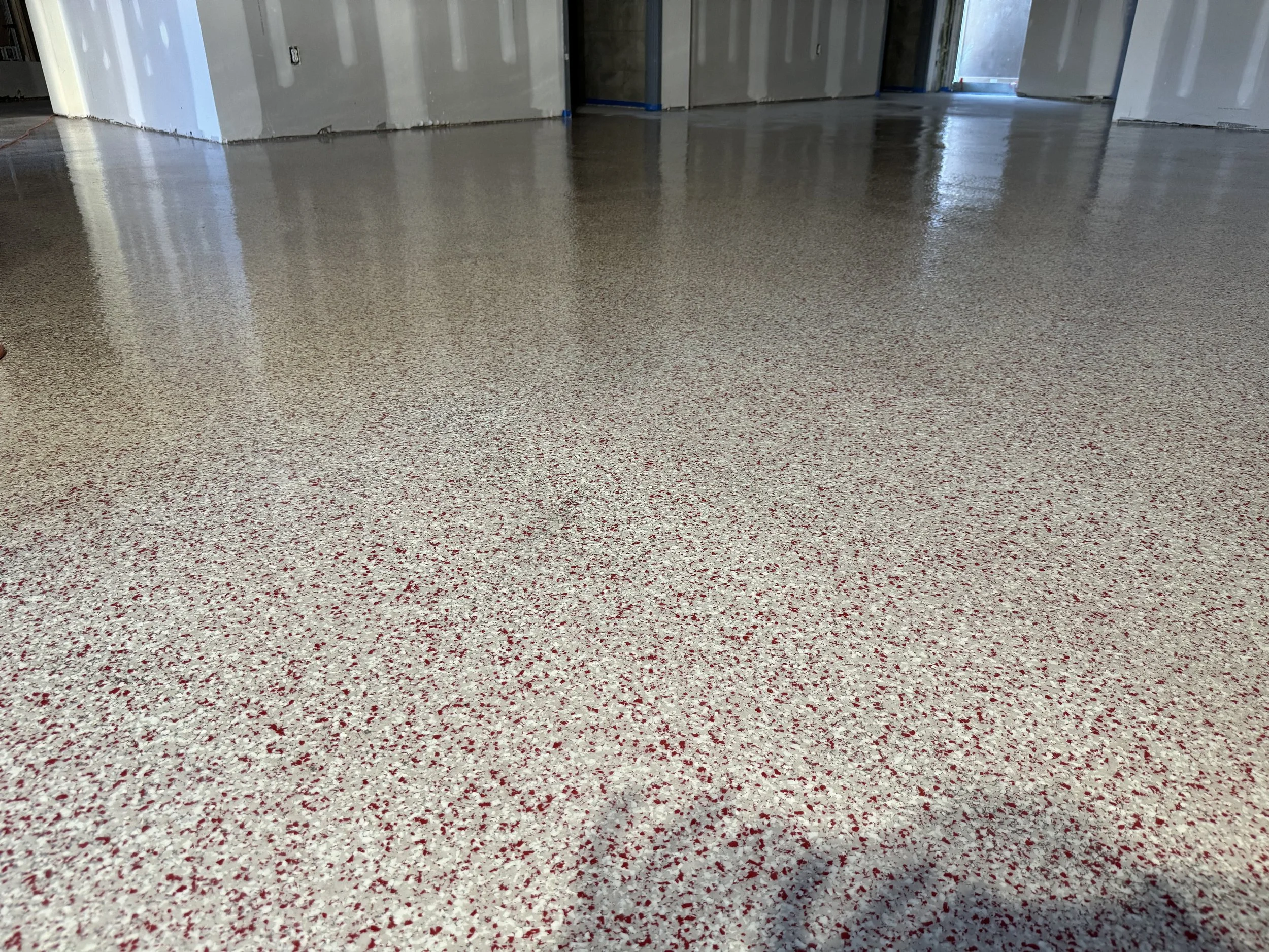 Polished terrazzo flooring in a room under construction with gray drywall walls and an open doorway.