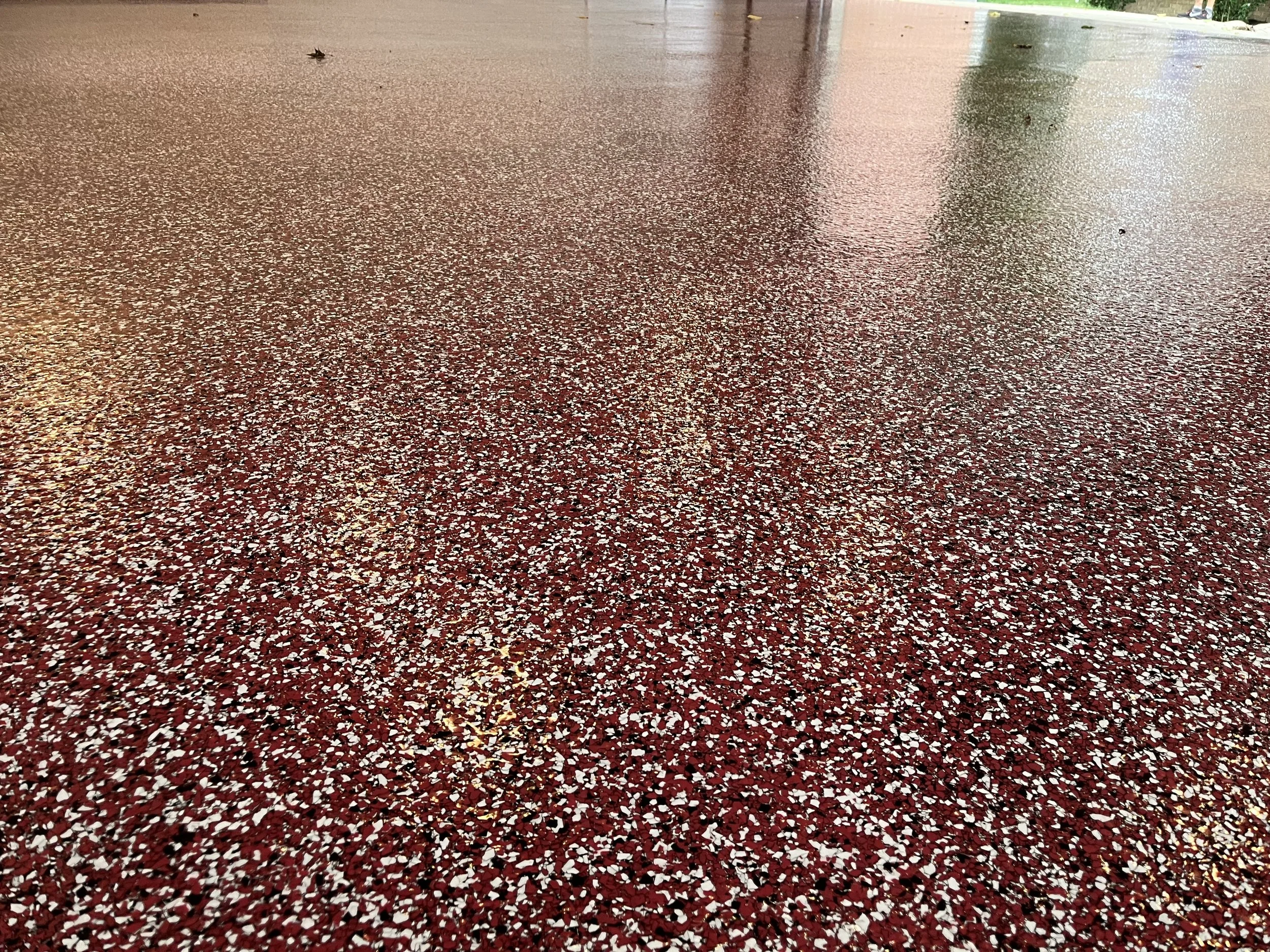 Red, black, and white terrazzo flooring with a reflective shiny surface, possibly outdoors or in a covered area.