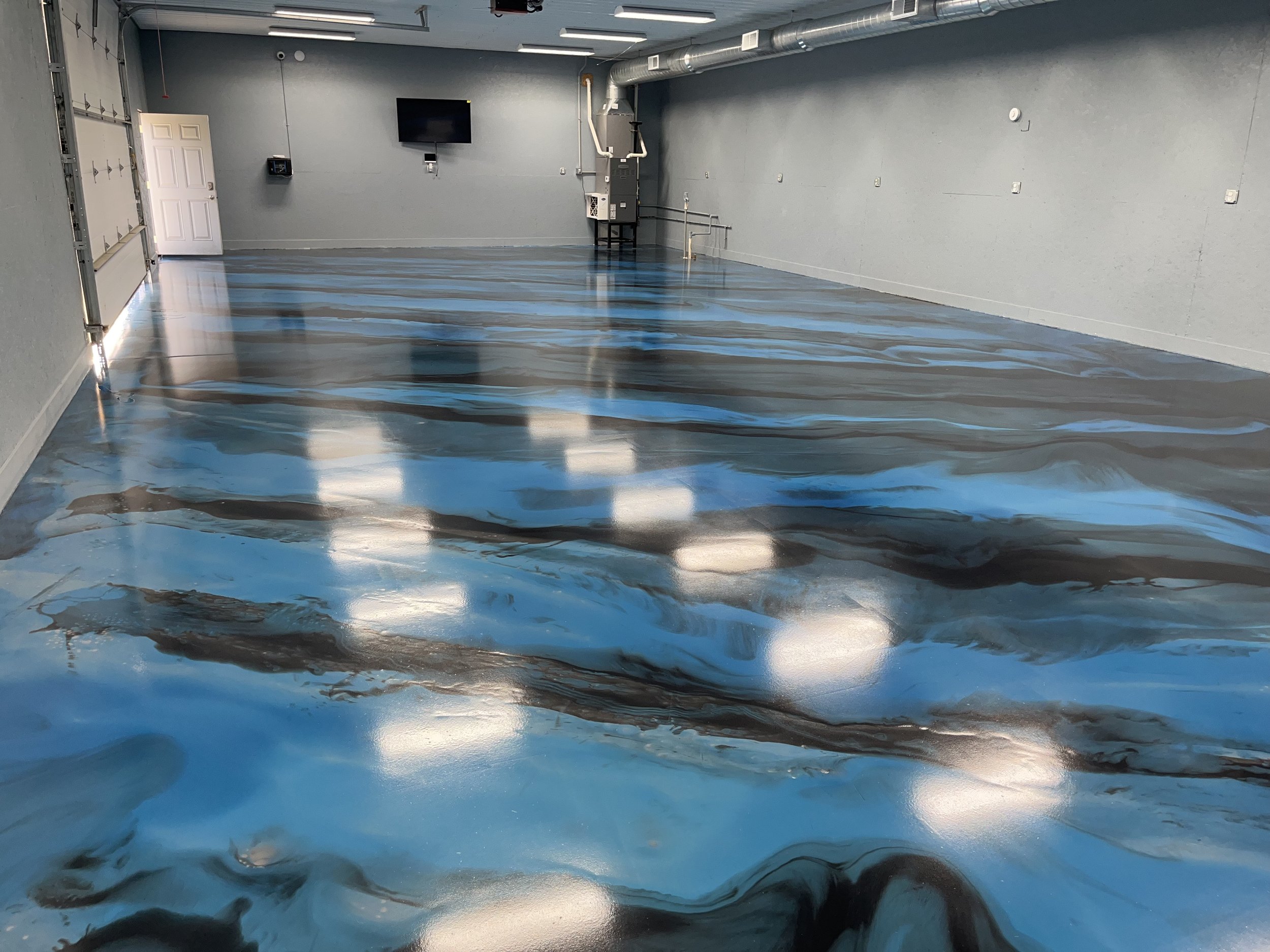 Empty garage with a marble-patterned epoxy floor in shades of blue, black, and white, with a white door, a TV, and grey walls.