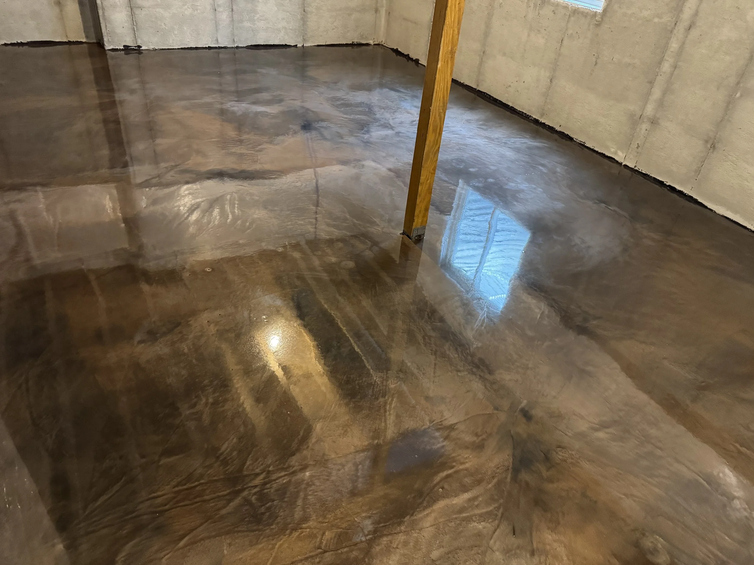 Polished concrete floor in an unfinished room with a yellow support post and a window reflecting on the surface.
