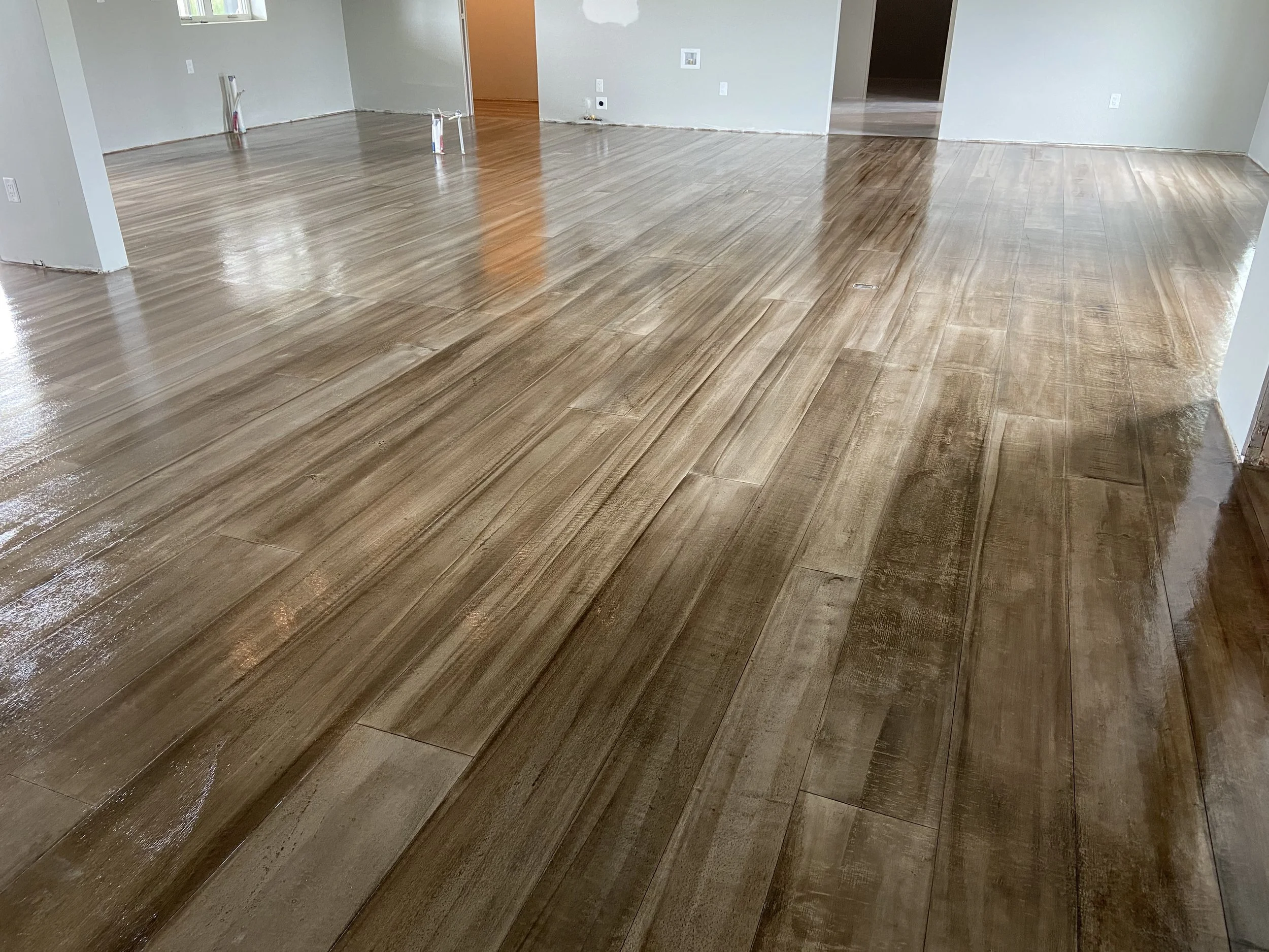 A room with newly installed hardwood flooring that is wet or freshly finished, with visible wood grain and a glossy surface, and some construction materials or tools visible near the walls.