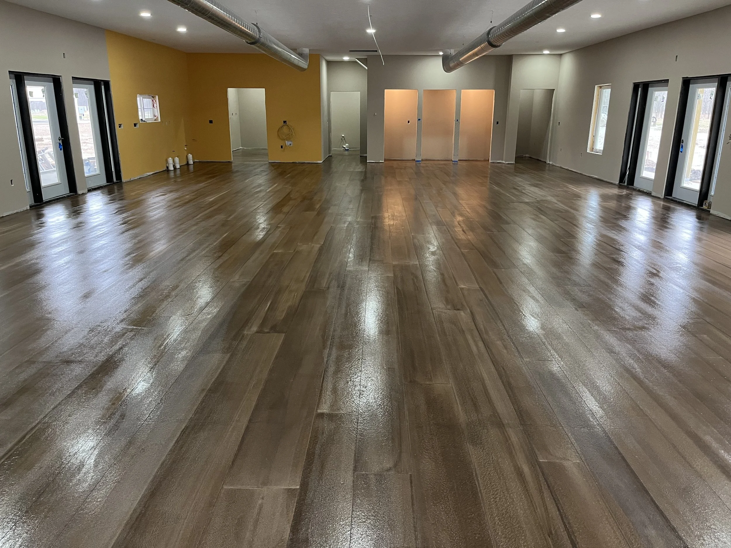 An empty room with shiny wooden flooring, multiple windows, and an open doorway leading to other rooms, with a yellow accent wall and unfinished walls.
