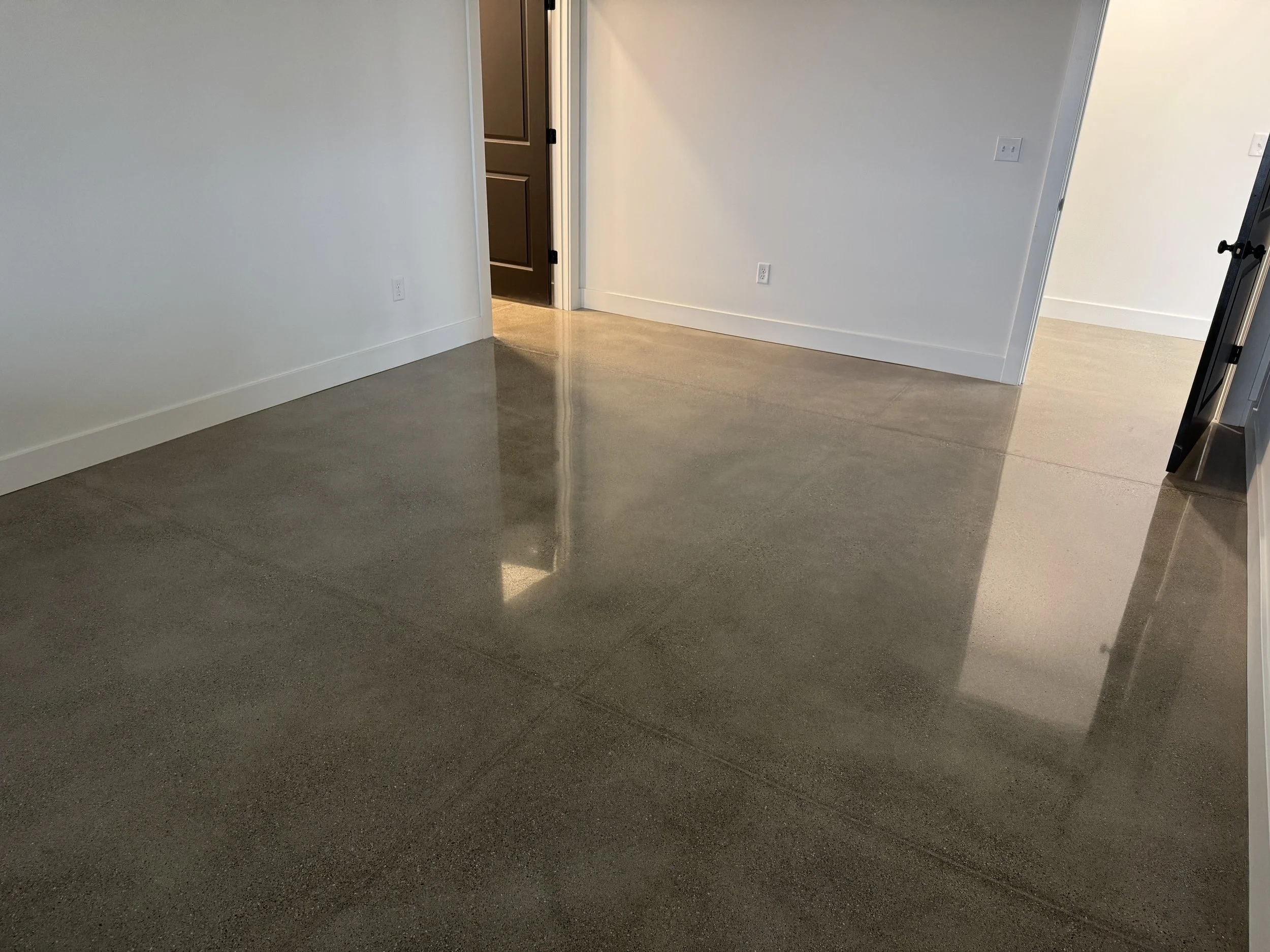 A room with polished concrete floors, white walls, multiple doorways, and electrical outlets.