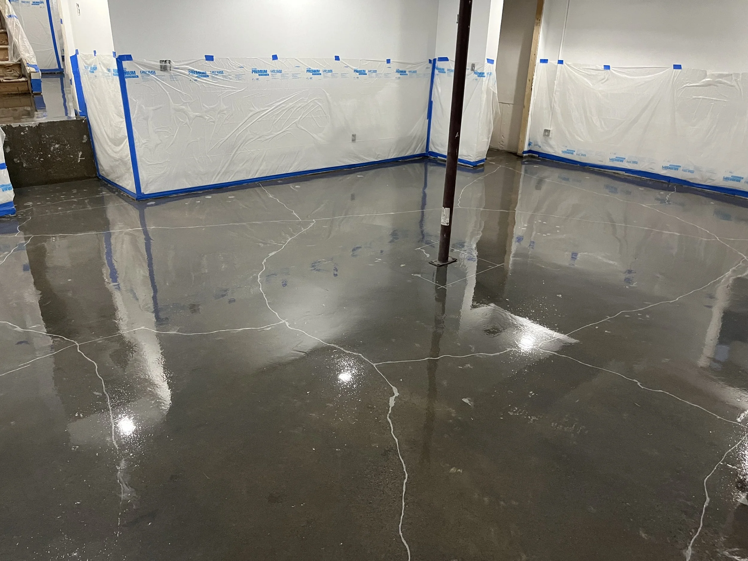 Interior of a building under renovation with a polished concrete floor, protected walls covered with plastic sheeting, and a temporary support pole in the center.