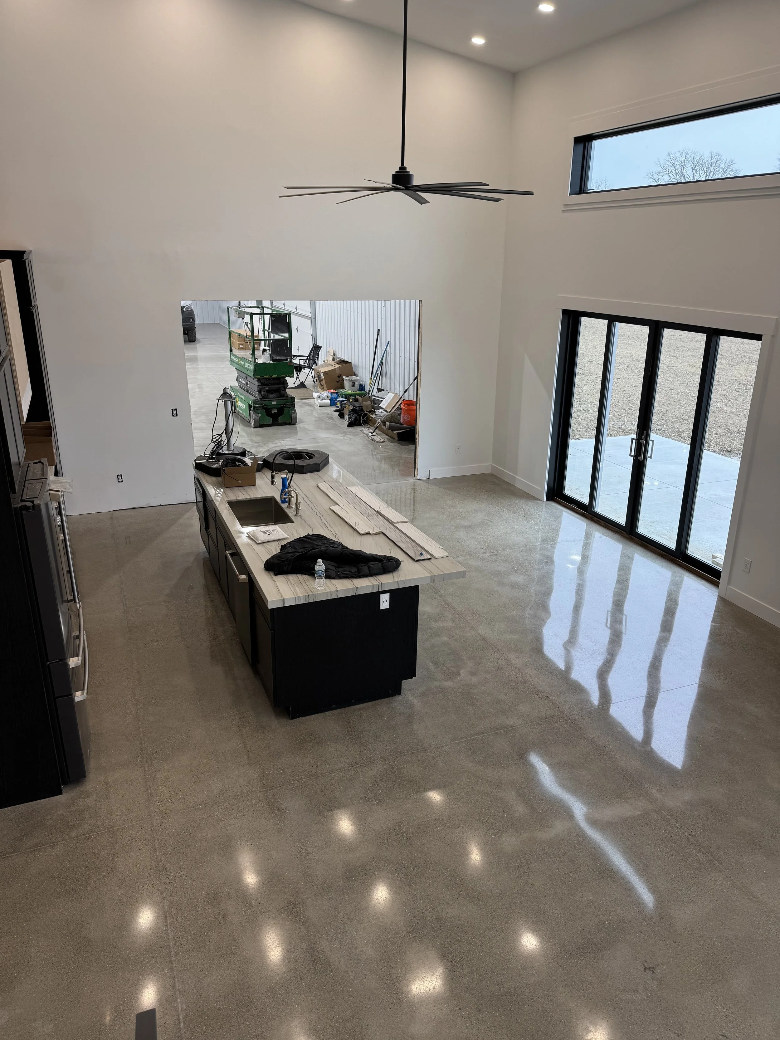 Empty modern kitchen with an island, large sliding glass door, and high ceiling with a ceiling fan, under construction or renovation.