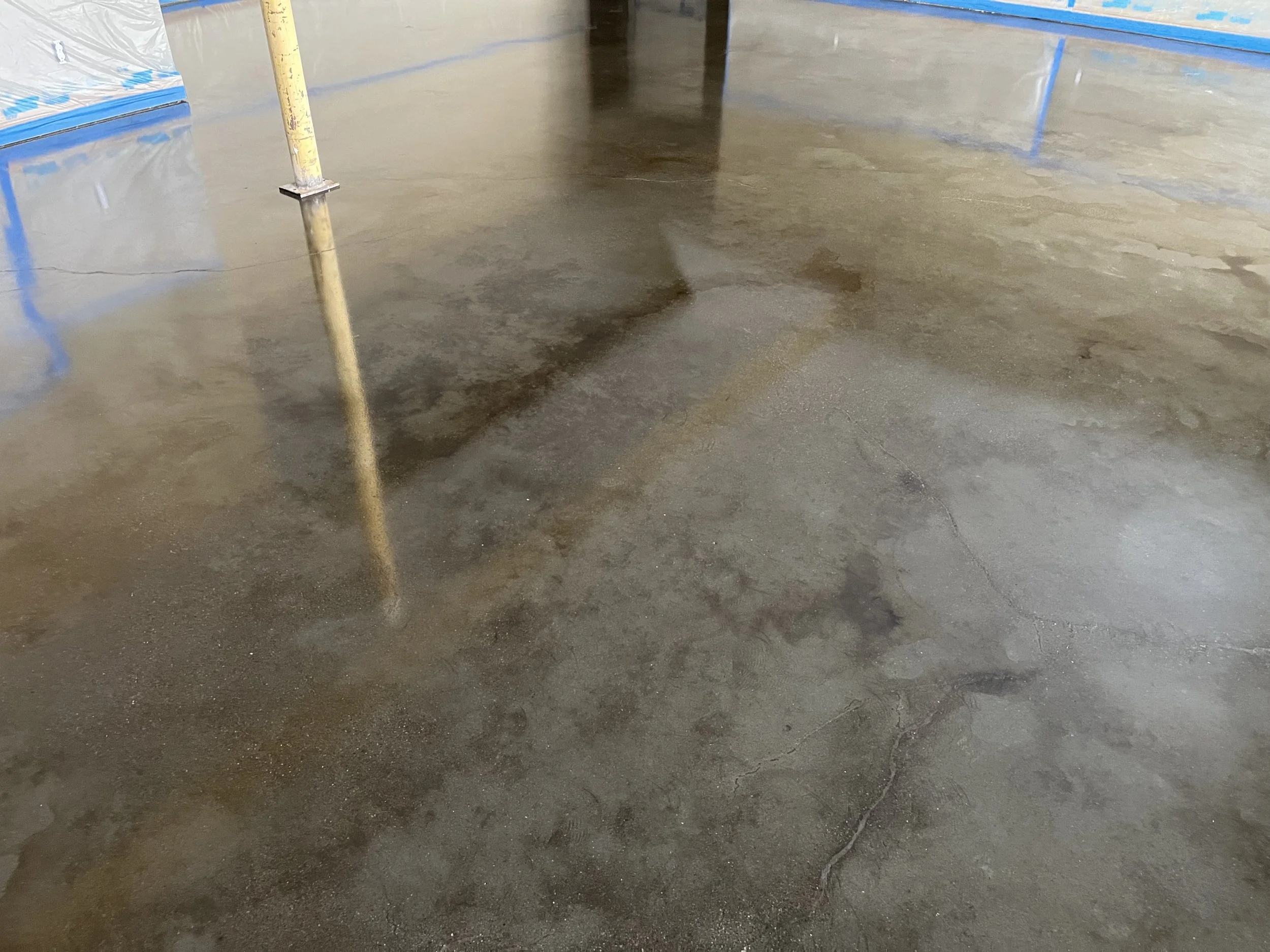 A concrete floor that appears to be damp or wet, with some cracks and uneven patches, in an indoor construction or renovation site.