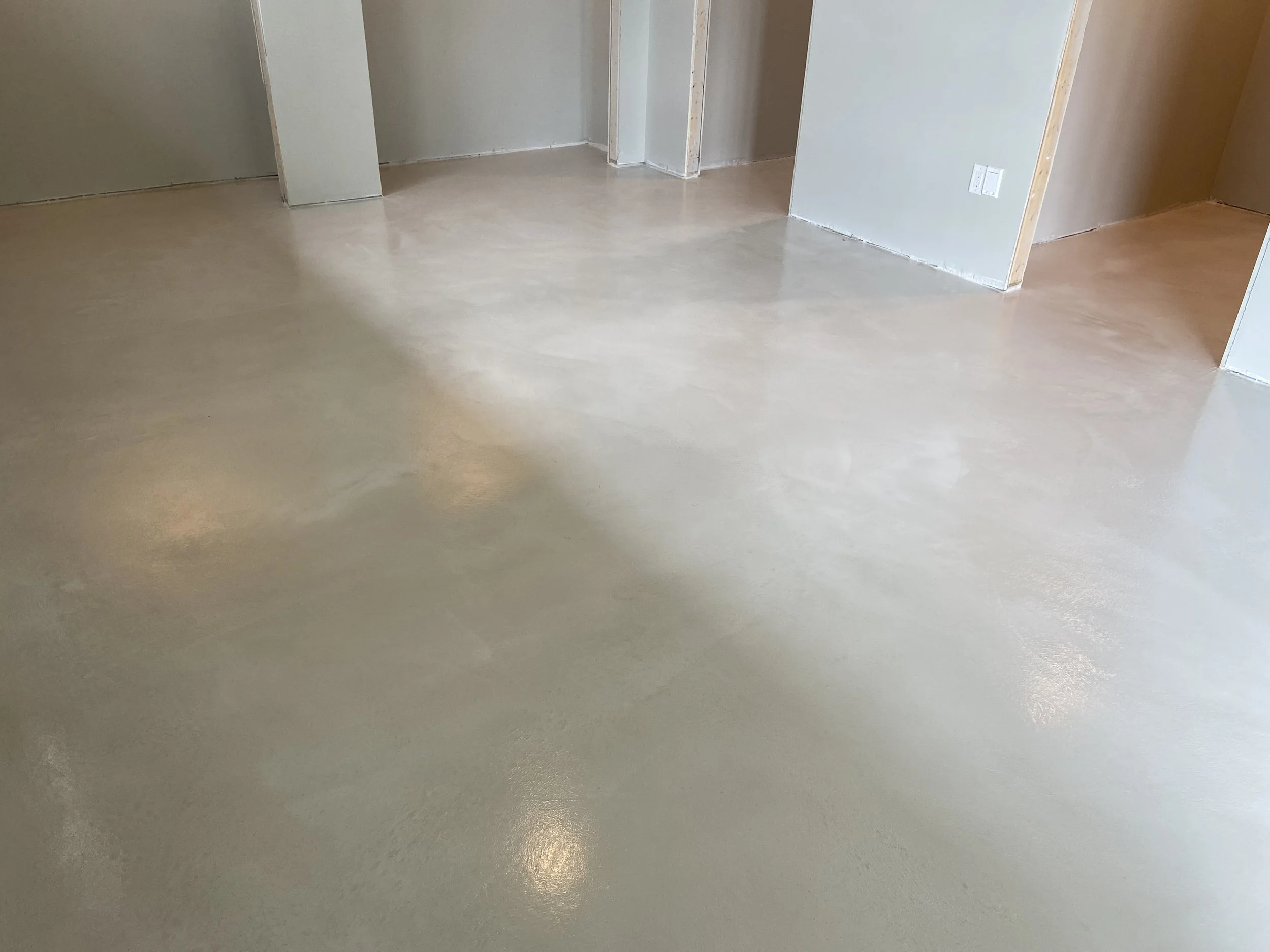 Interior of a room with freshly finished beige or light tan polished concrete floors, with unfinished walls and door openings.