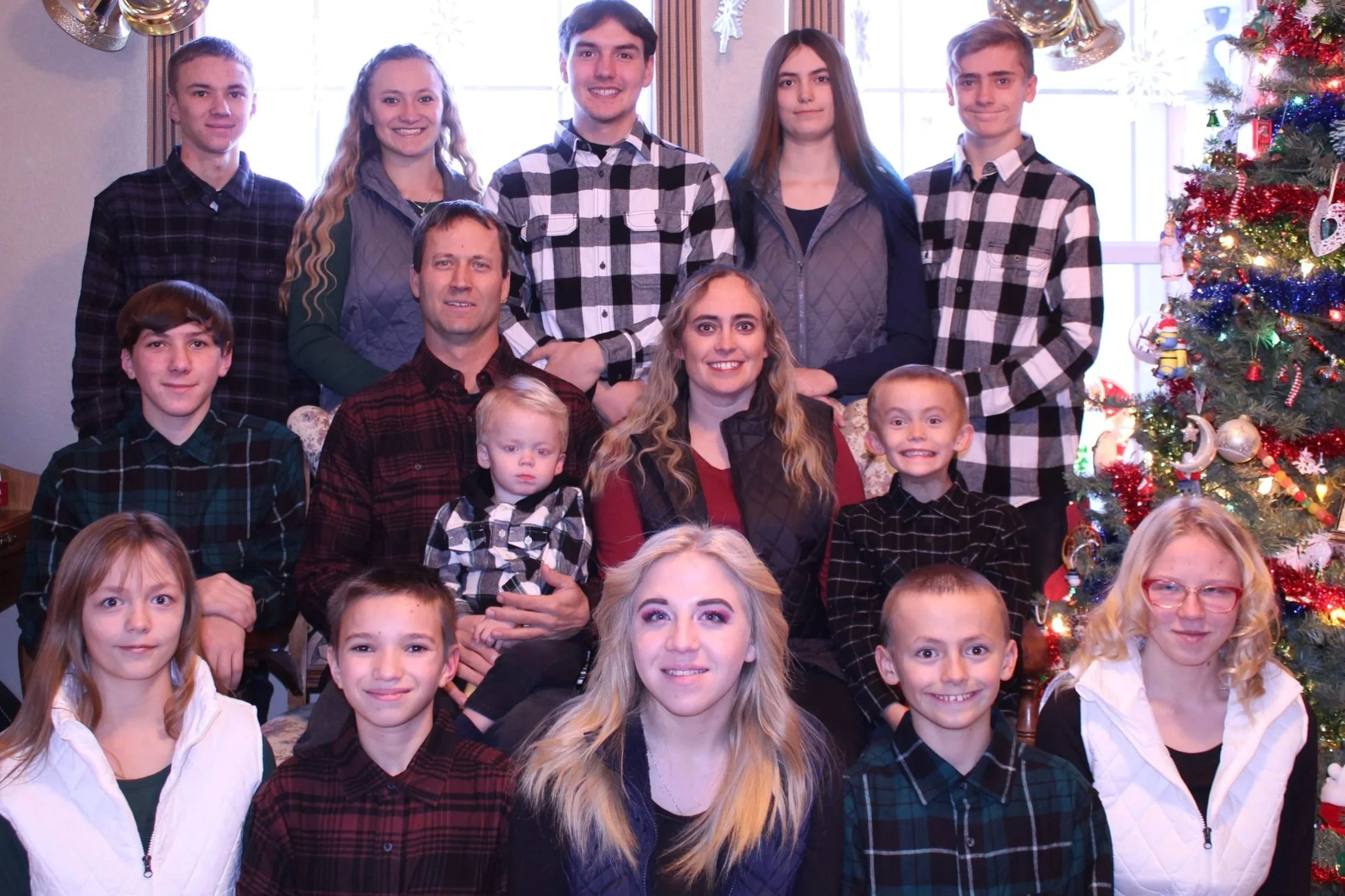 A large family photo taken indoors with Christmas decorations, including a decorated Christmas tree, with seventeen people of various ages smiling and posing together.