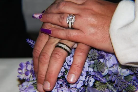 Close-up of a person's hands with rings, resting on purple flowers.