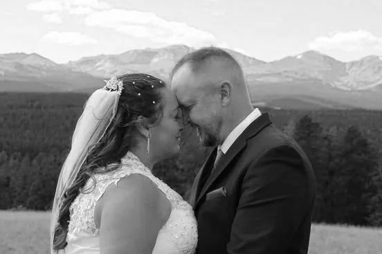 A bride and groom standing closely with foreheads touching in an outdoor setting with mountains in the background.