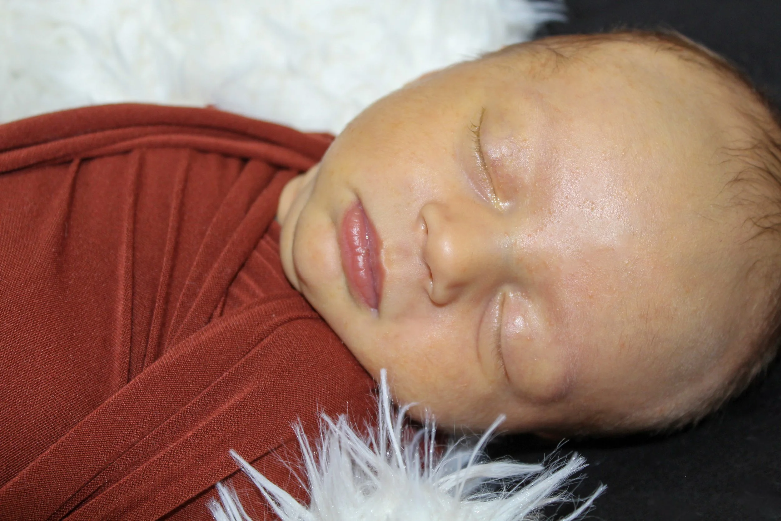 Close-up of a sleeping baby with closed eyes, wearing a red garment, lying on a soft surface.