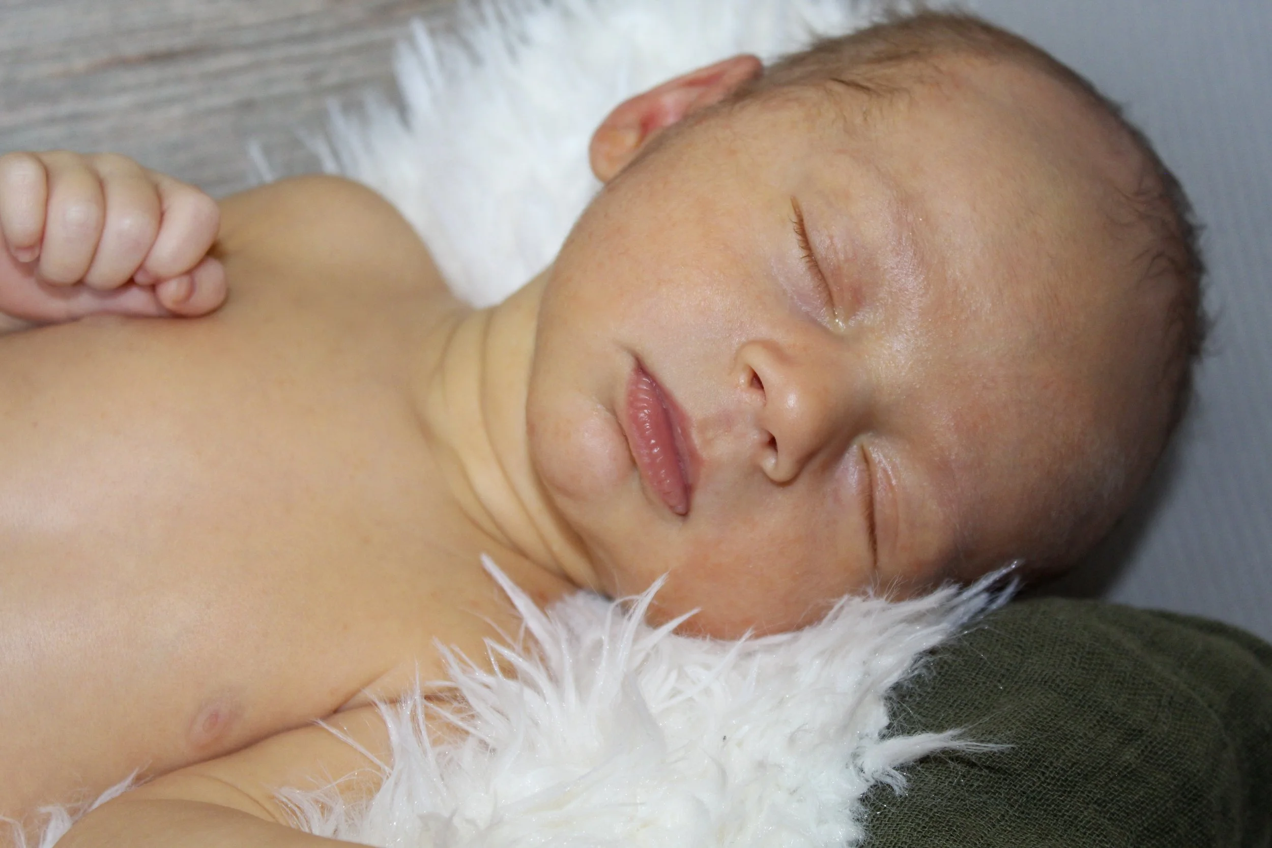 Close-up of a sleeping newborn baby lying on a fluffy white blanket, with a wooden surface in the background.