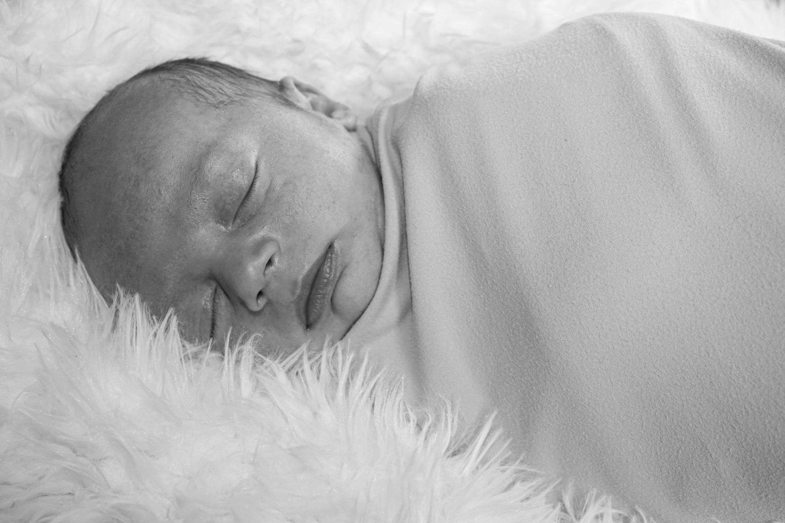Close-up of a newborn baby sleeping on a fluffy surface with a blanket.