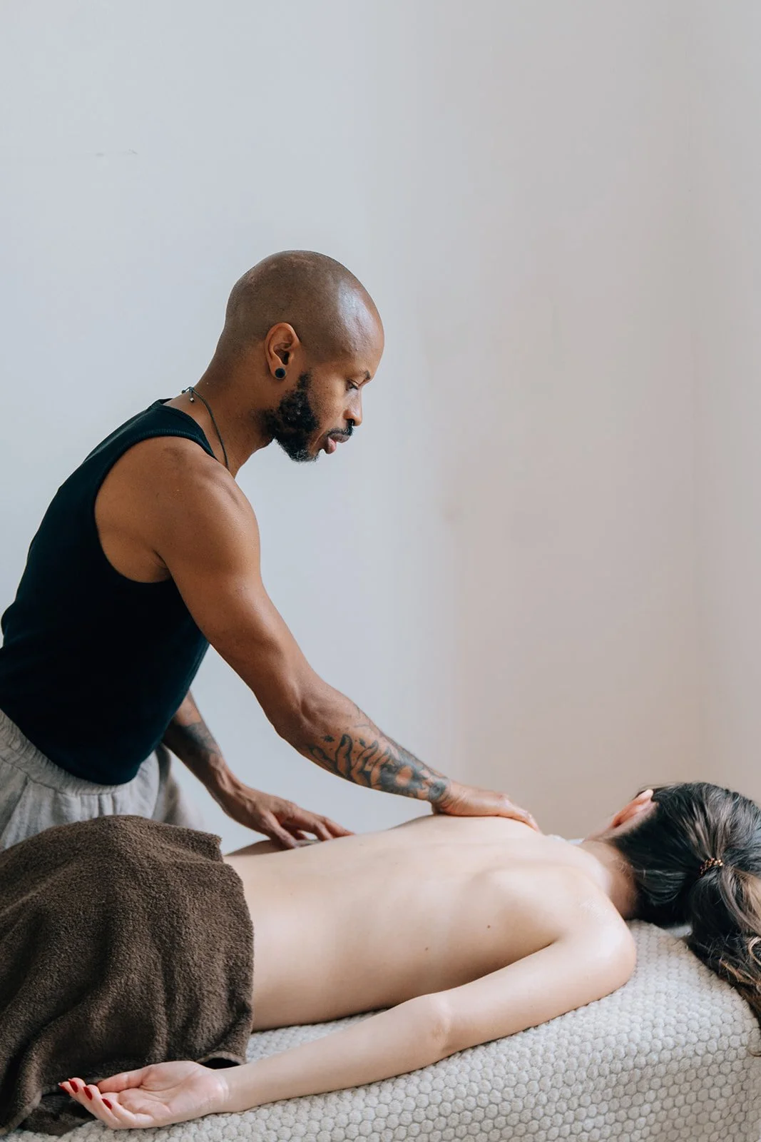 Un homme donne un massage à une femme allongée sur une table, vue de profil, dans une pièce claire.