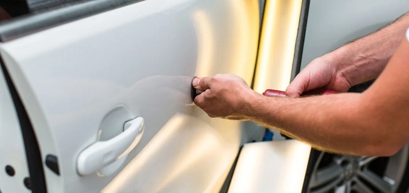 Un technicien qui répare une bosse causée par un coup de portière en débosselage sans peinture