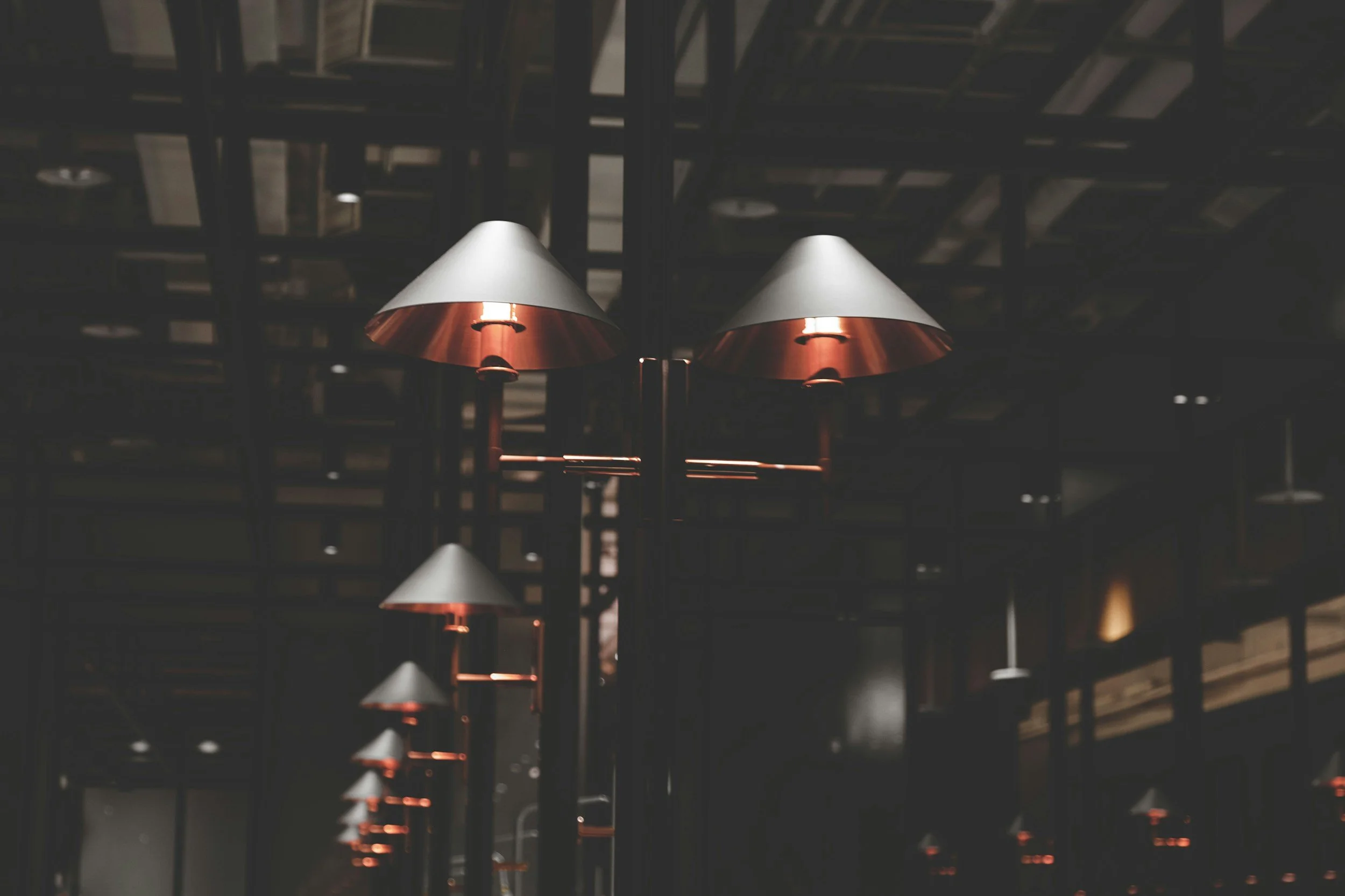 Multiple ceiling lamps with metallic shades hanging in a dimly lit interior space, possibly a restaurant or cafe.