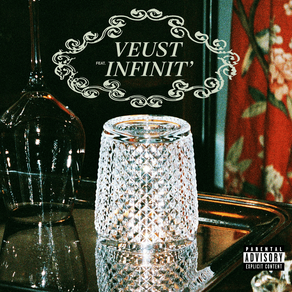 Une couverture d'album avec un verre en cristal, une bouteille en verre sombre, et un fond décoratif rouge avec des motifs floraux. Le titre "VEUST INFINIT' feat." est inscrit dans un cadre ornemental blanc, avec un label ¡Parental Advisory! en bas à