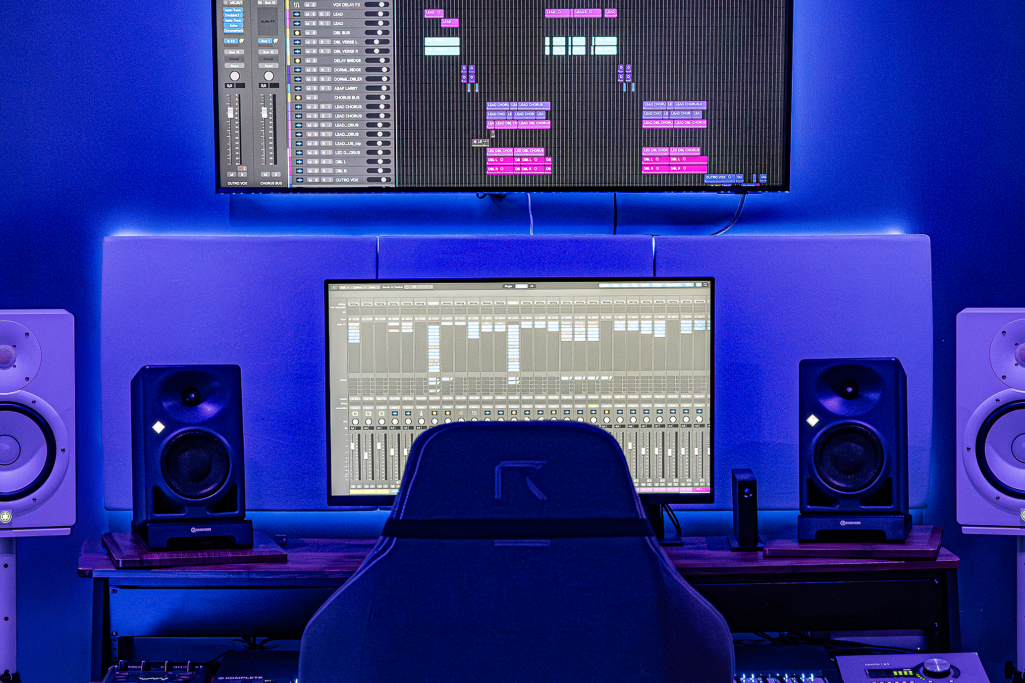 Studio d'enregistrement NPL Studio avec deux écrans, haut-parleur, clavier et fauteuil, ambiance éclairée en bleu.