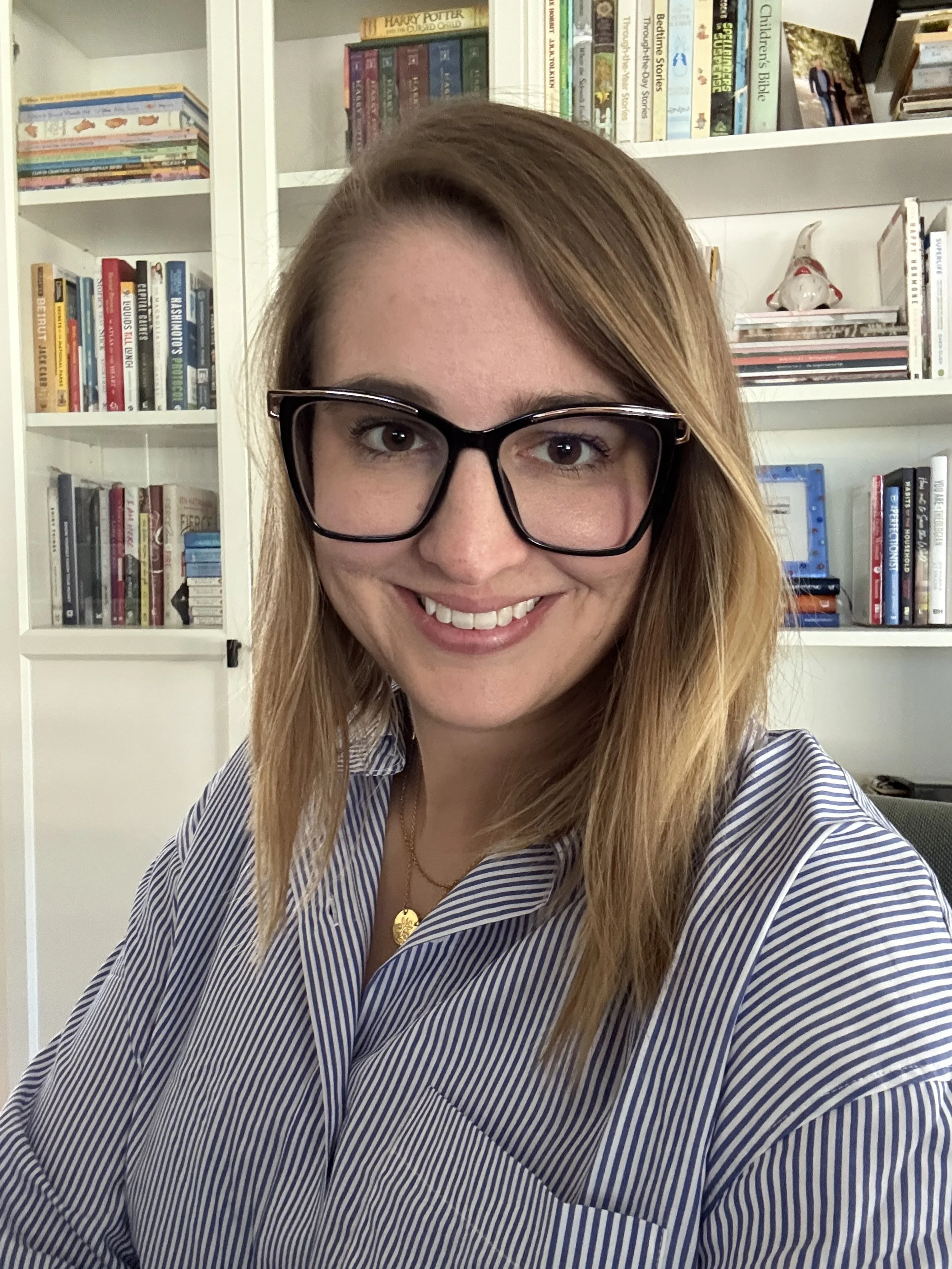 A photo of Samantha Mans, wearing blue stripped blouse and glasses.