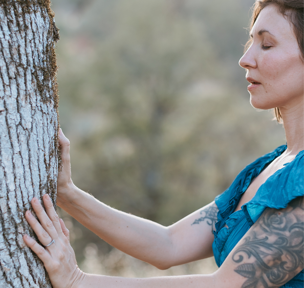 Elena presses her hands against a tree trunk outdoors, seeking to connect with the tree's spirit, spirit guides, and inner wisdom.