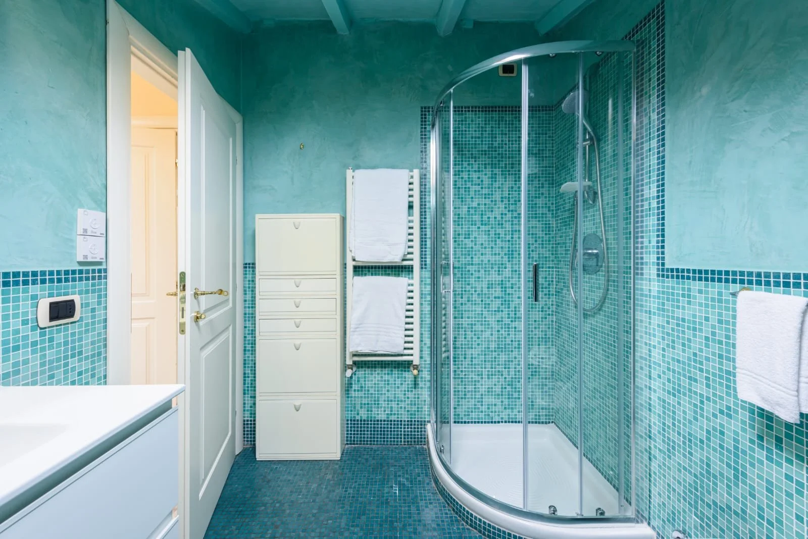 Another image of a blue tiled bathroom & toilet, showing the shower