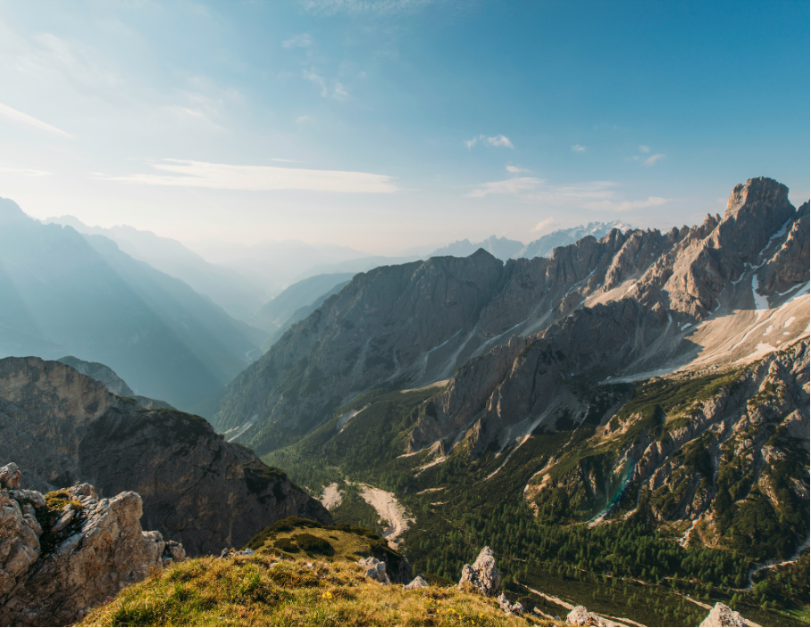 Berglandschaft mit hohen, schneebedeckten Gipfeln, grünen Tälern und einer weiten, blauen Himmelslandschaft