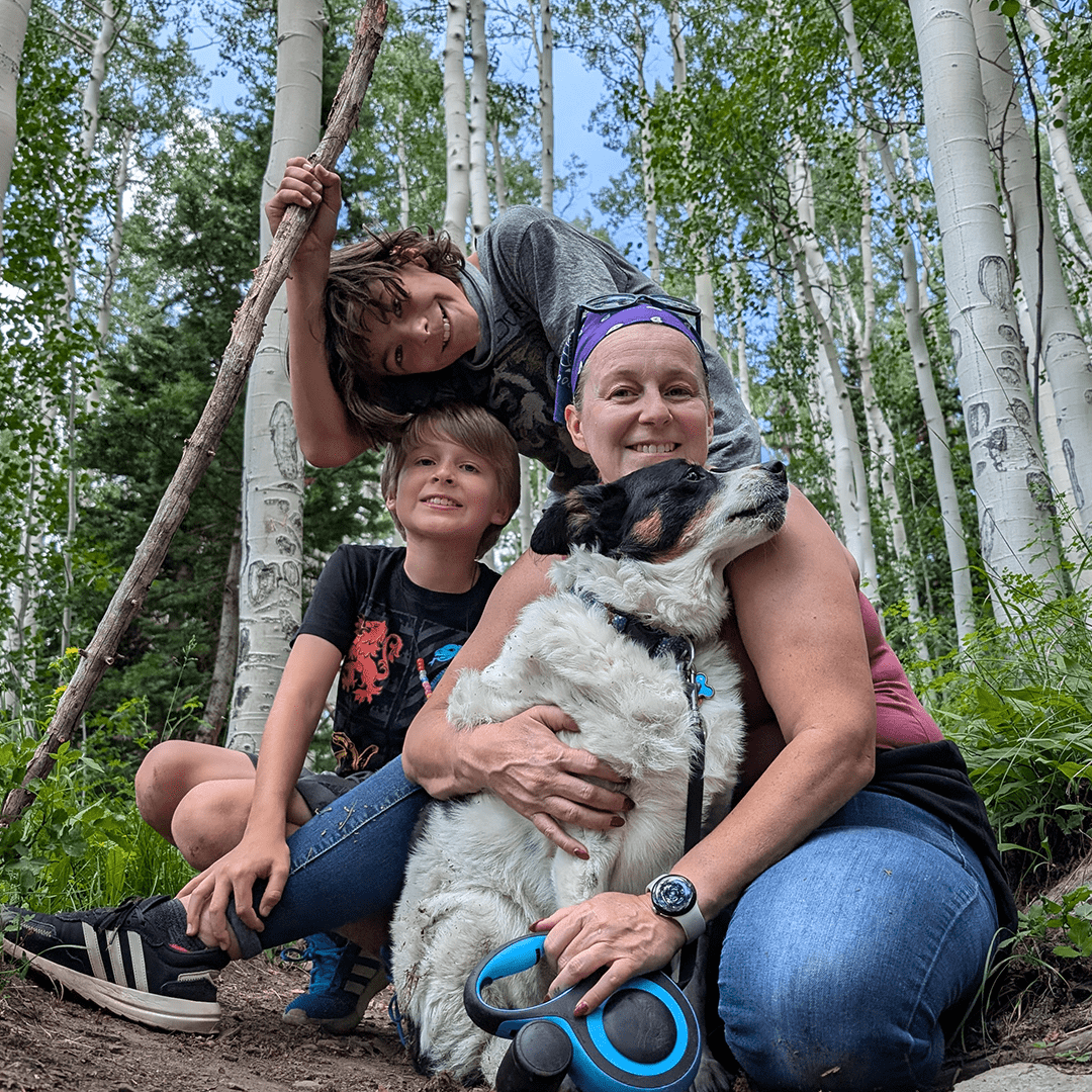 Three people, a woman, a boy, and a girl, with a dog in a forest of aspen trees during daytime.