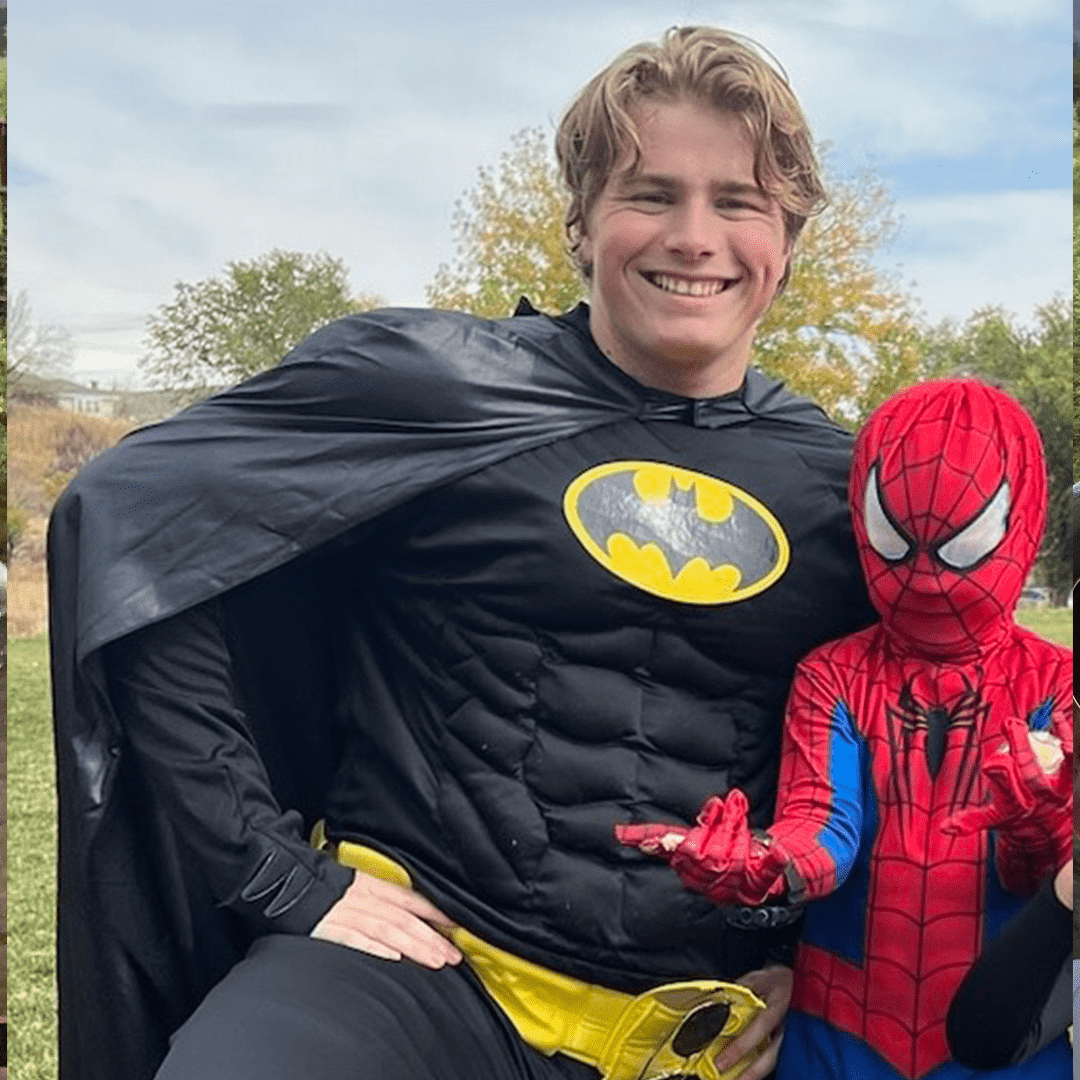 A young man dressed as Batman and a child dressed as Spider-Man posing outdoors on a fall day.