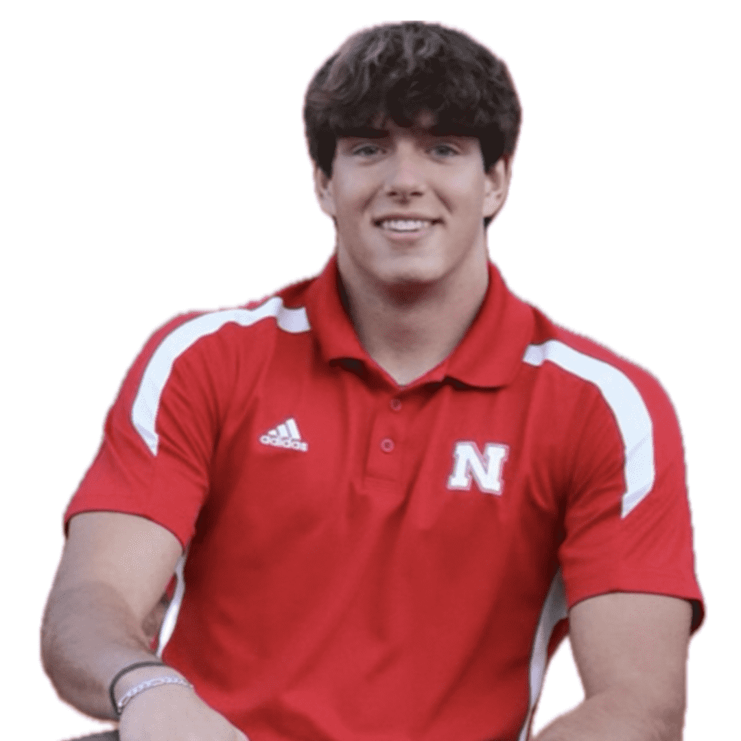 Young man wearing a red sports shirt with a white 'N' and Adidas logo, smiling, with dark curly hair.