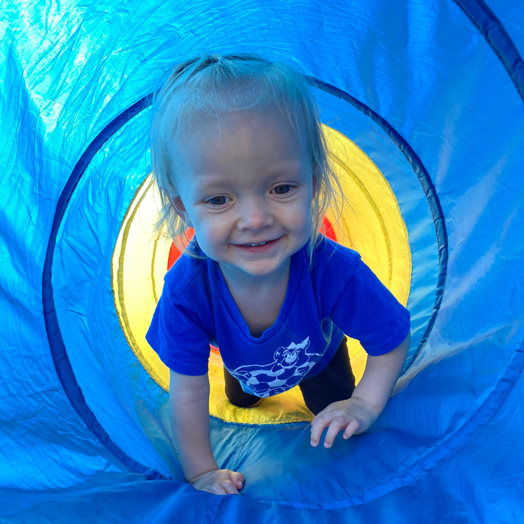 Young girl in a blue shirt crawling through a colorful playground tunnel.