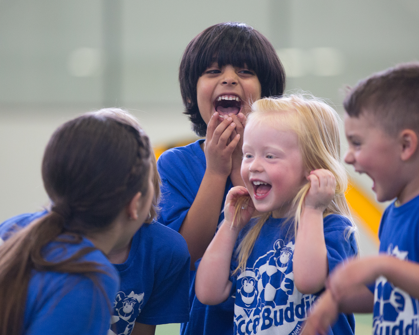 Children in blue sports shirts laughing and smiling together indoors.