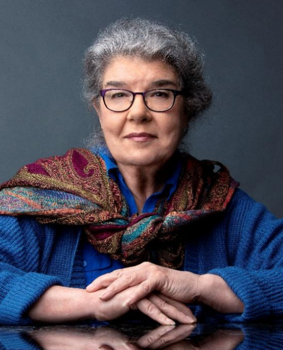 artist portrait headshot of Linda Williams McCune wearing glasses with her hair up and a near smile. She's wearing a blue terrycloth looking sweater and a silk scarf tied loosely around her neck, off her right shoulder.