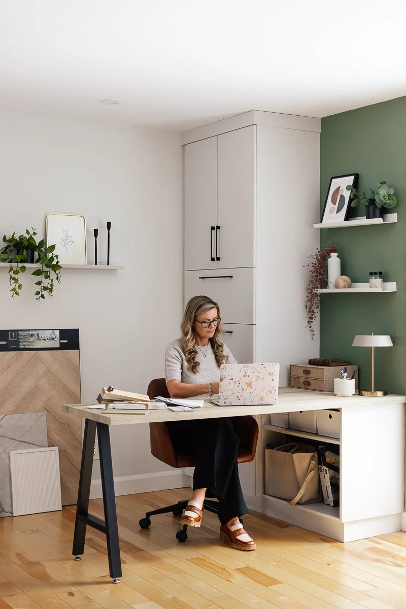 Femme travaillant à un bureau dans une pièce moderne avec des étagères, des plantes et des décorations.