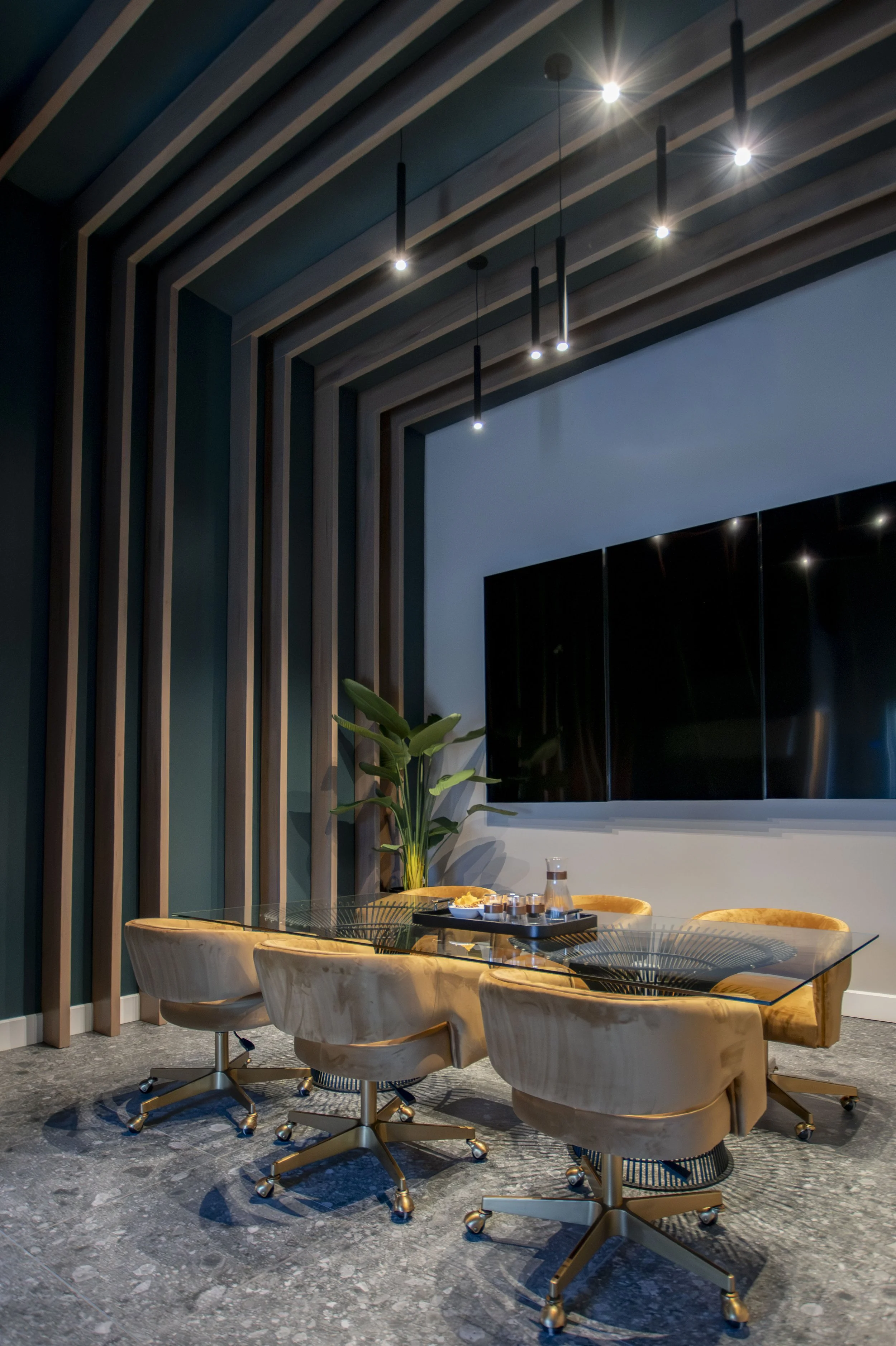 Une salle de réunion moderne avec un grand écran derrière une table en verre. Six fauteuils en cuir beige sont placés autour. Un plant vert est placé à côté de l'écran, et des meubles avec des objets sont visibles sur la table.