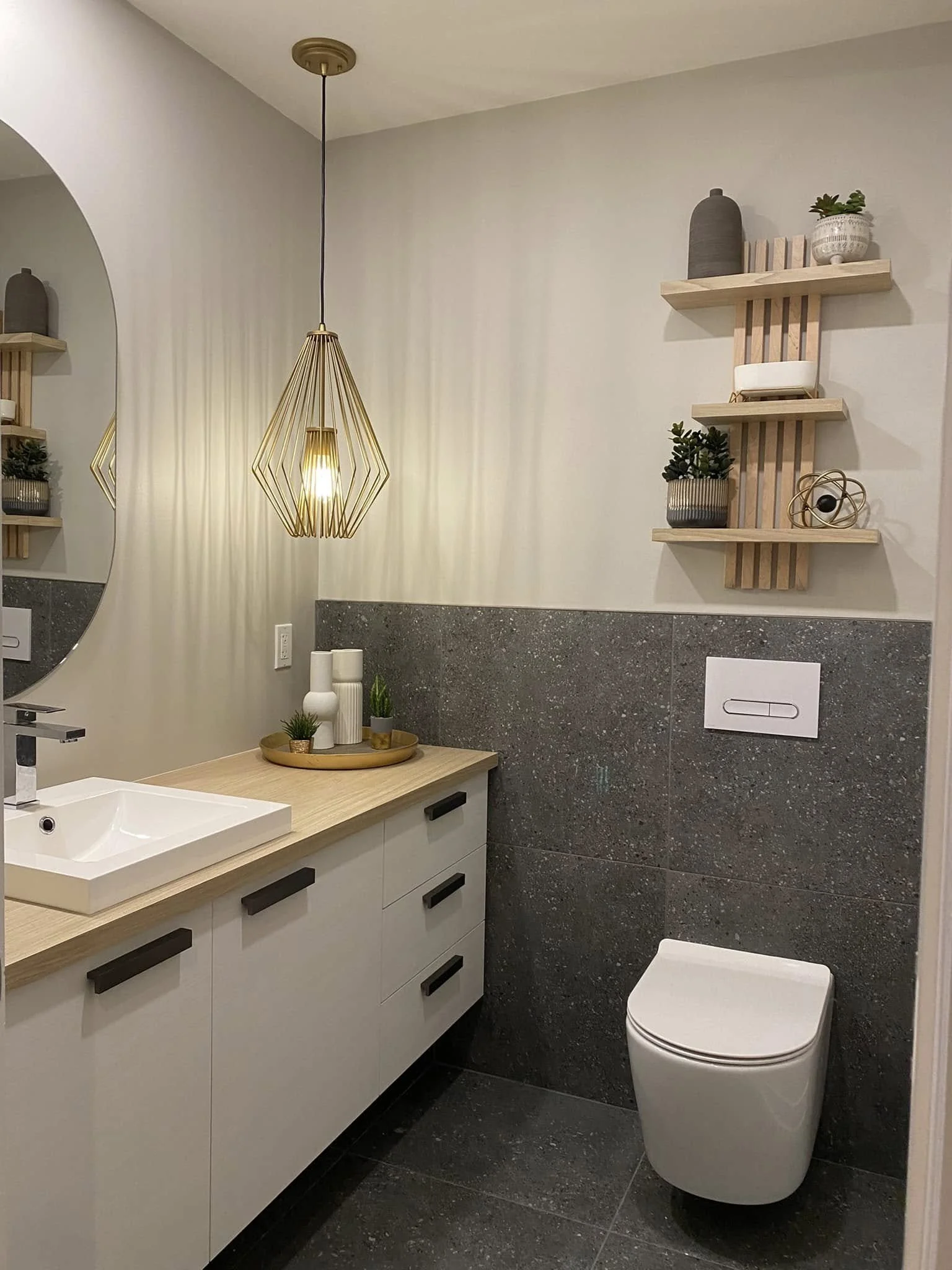 Une salle de bain moderne avec un lavabo blanc, un miroir rond, une armoire de rangement avec des plantes et des décorations. Pièce complètement rénovée pour un look moderne, mais intemporel.