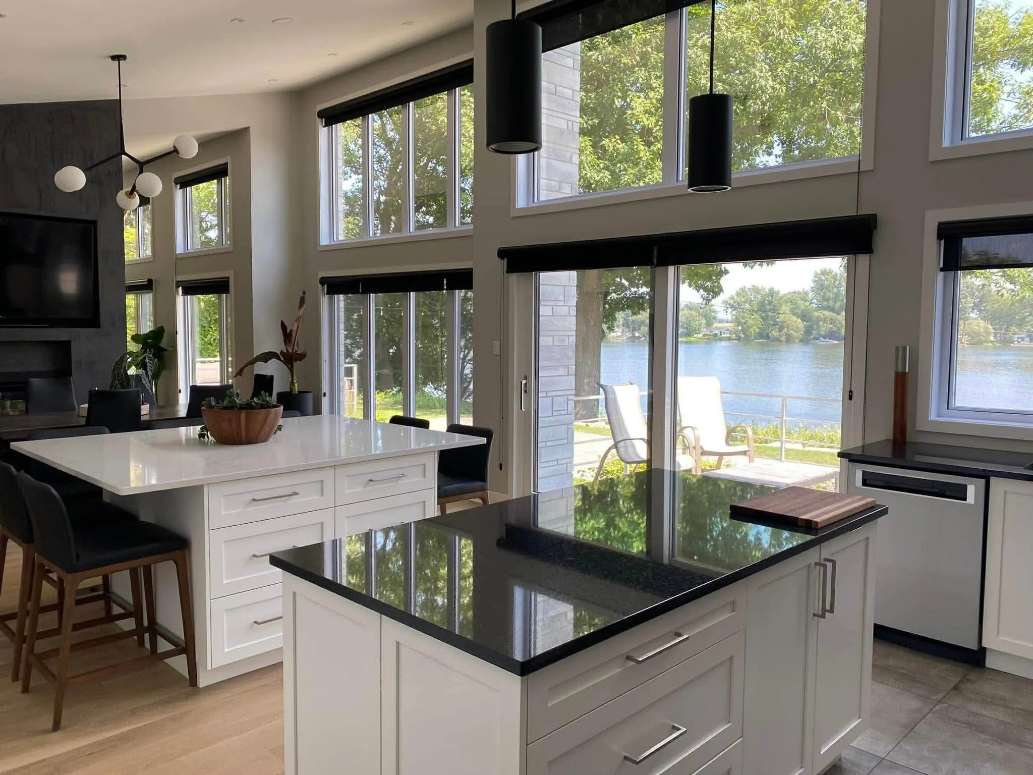 Cuisine moderne avec une vue sur le lac, grande île blanche, comptoir noir, fenêtres hautes laissent entrer beaucoup de lumière, décoration minimaliste.