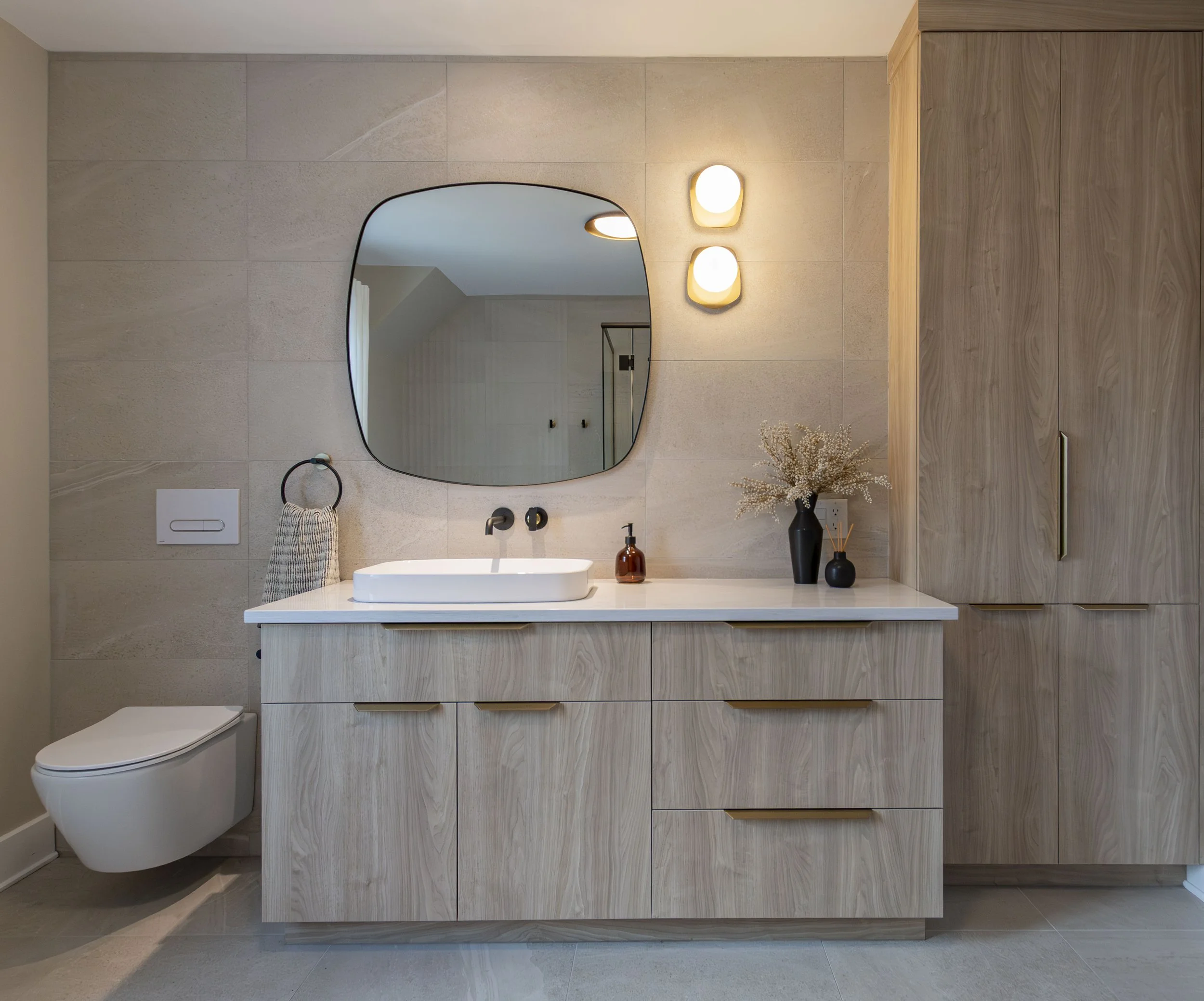 Un mur de salle de bain avec un miroir, un lavabo, une plante et deux appliques lumineuses.