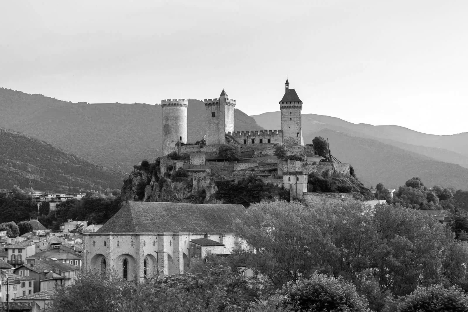 Château médiéval perché sur une colline avec montagnes en arrière-plan, vue depuis la ville en contrebas.