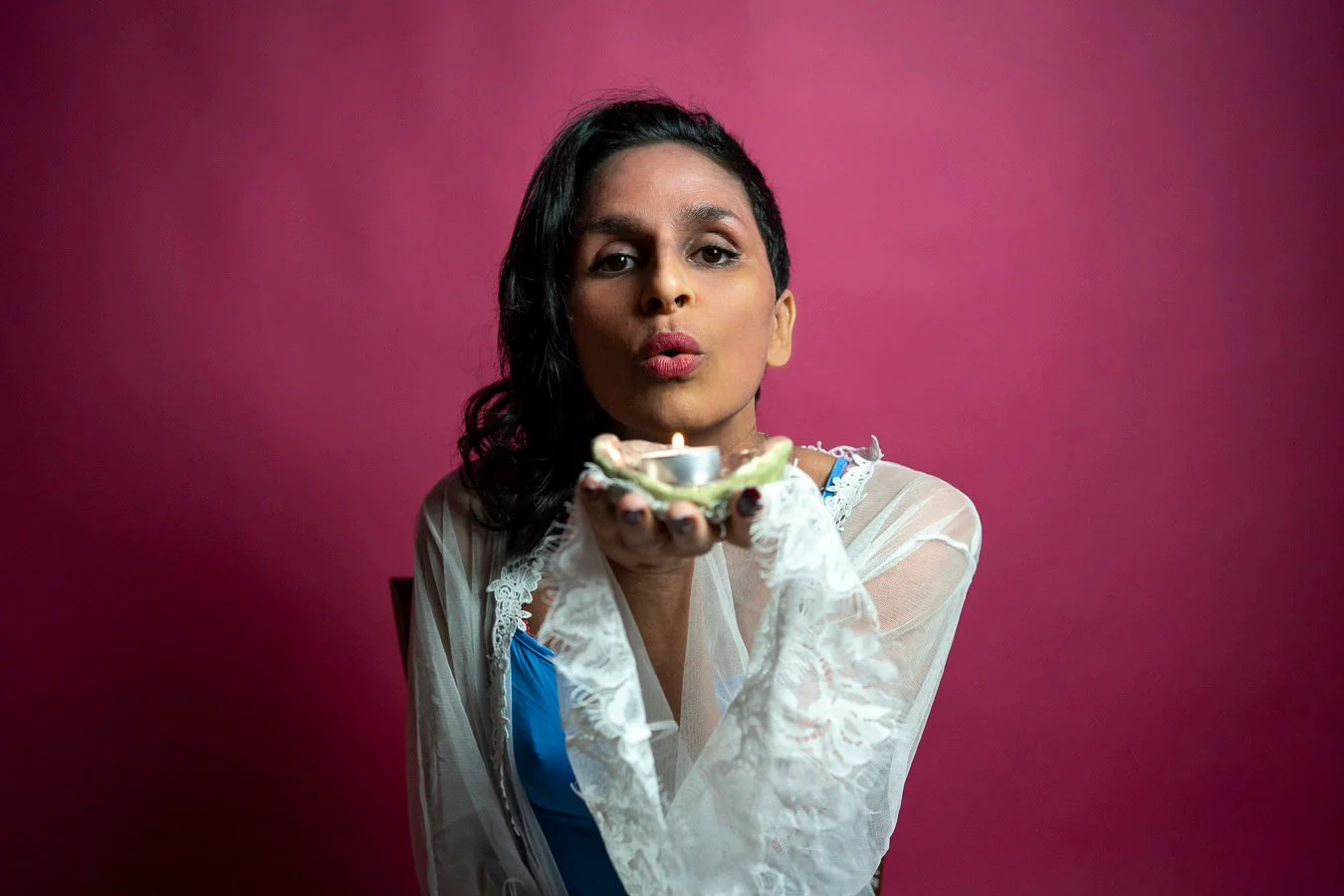 A woman blowing out a birthday candle on a cupcake with purple background.