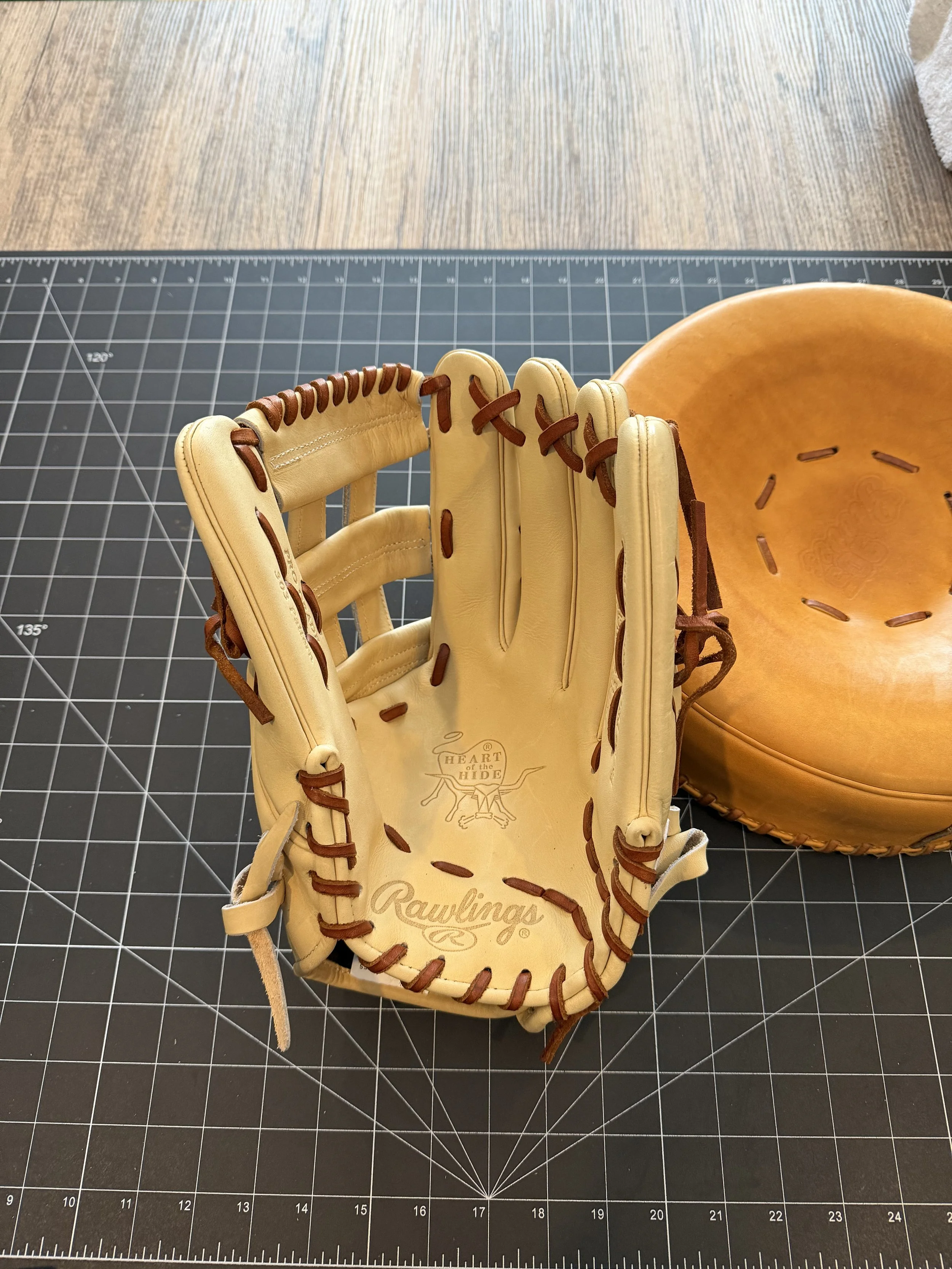 A Rawlings baseball glove with brown laces placed next to a brown leather baseball catcher's mitt on a black cutting mat.