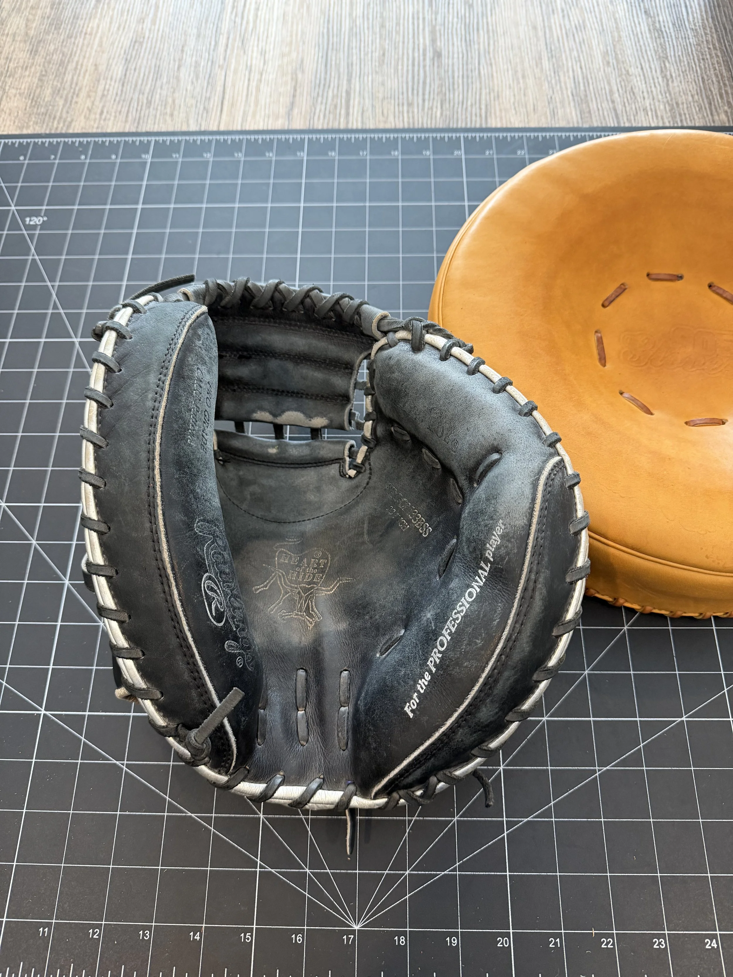 A black baseball glove and a brown baseball mitt on a black cutting mat with white grid lines.