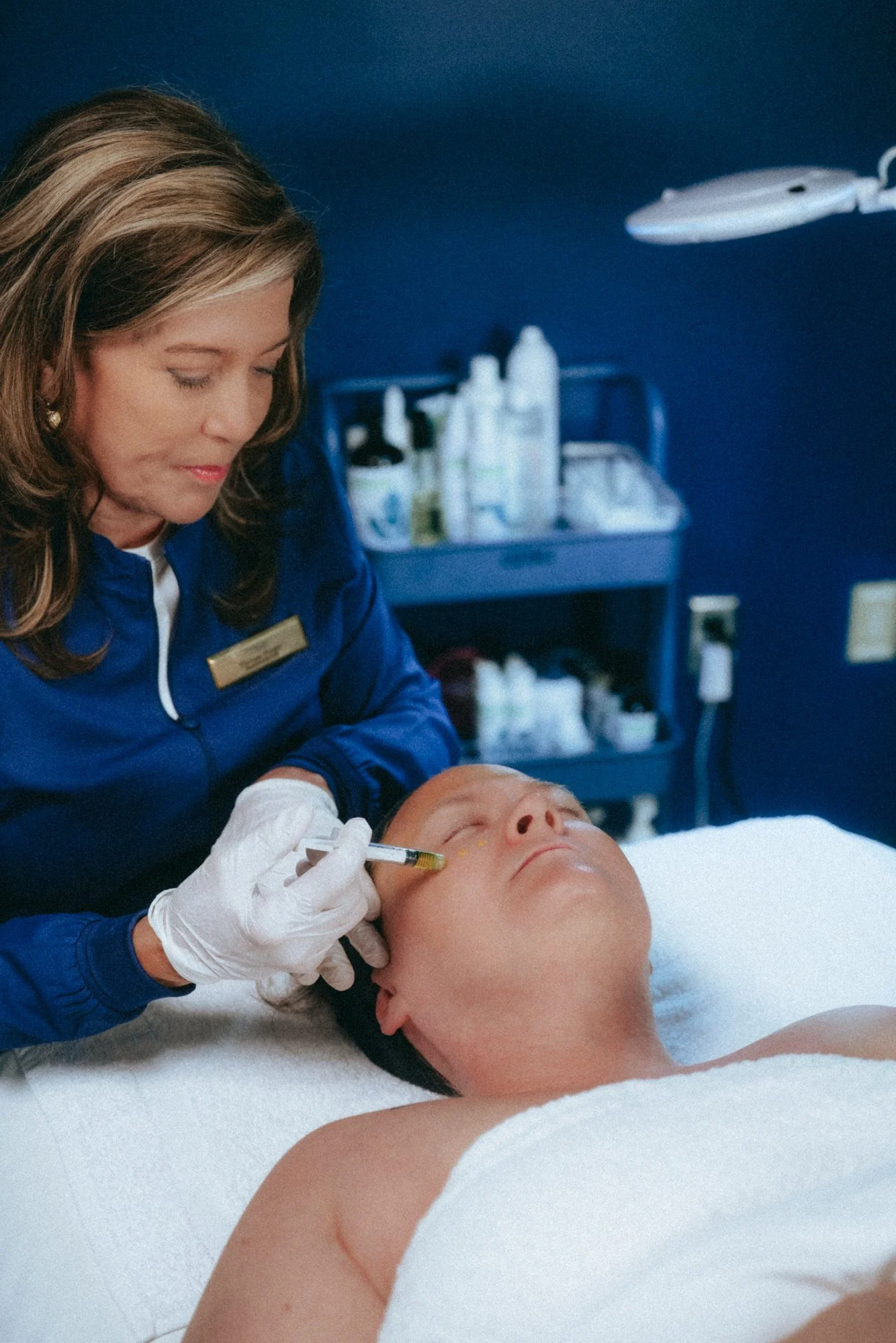 A woman receiving facial skincare treatment from a professional in a spa or clinic setting.