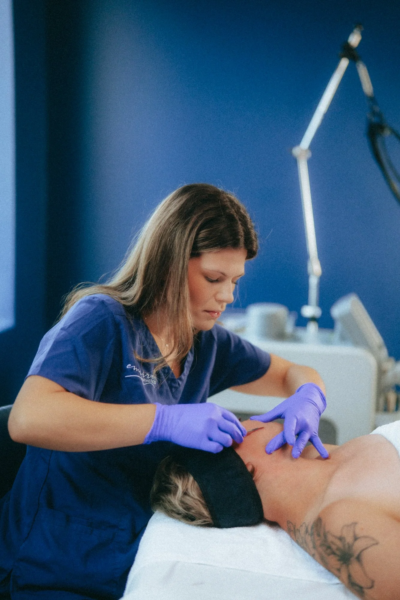 A medical professional wearing purple gloves is performing a procedure on a person's neck in a clinical setting with blue walls.