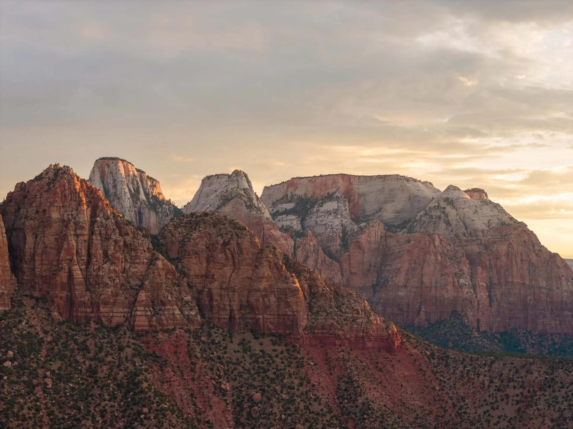 Sunset over colorful layered mountains with red, orange, and white rock formations and a cloudy sky.