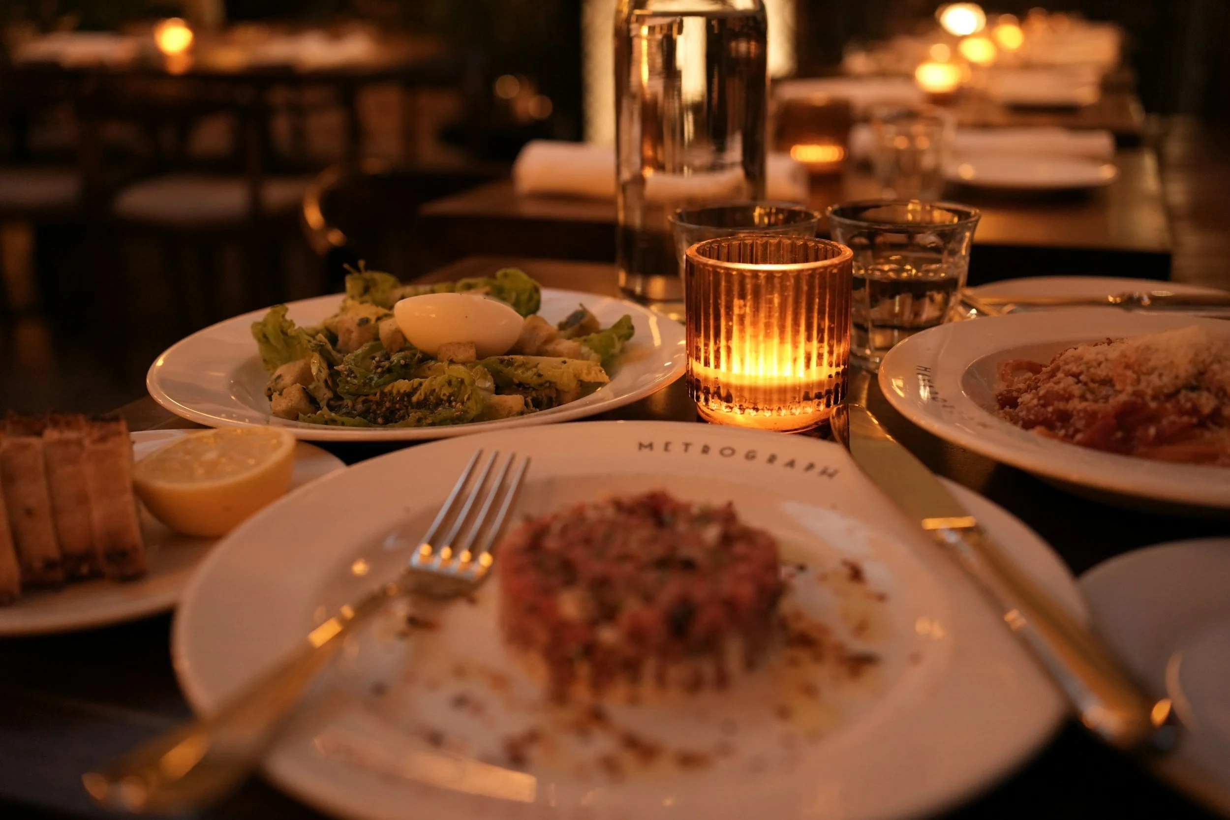 A warmly lit restaurant table set with plated dishes, drinks, and candlelight, illustrating a relaxed dinner during a romantic getaway near Zion National Park.